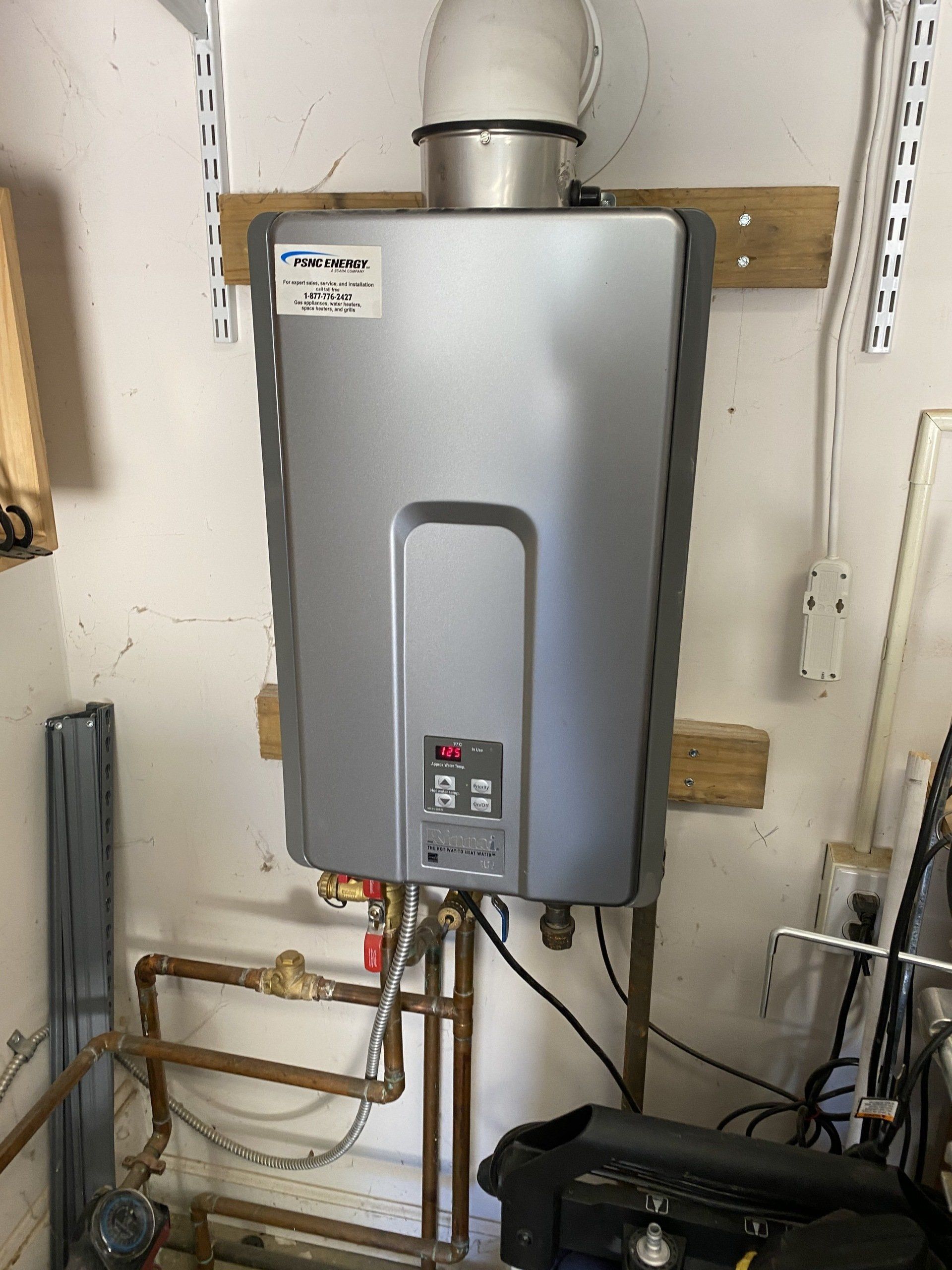A water heater is hanging on a wall next to pipes.