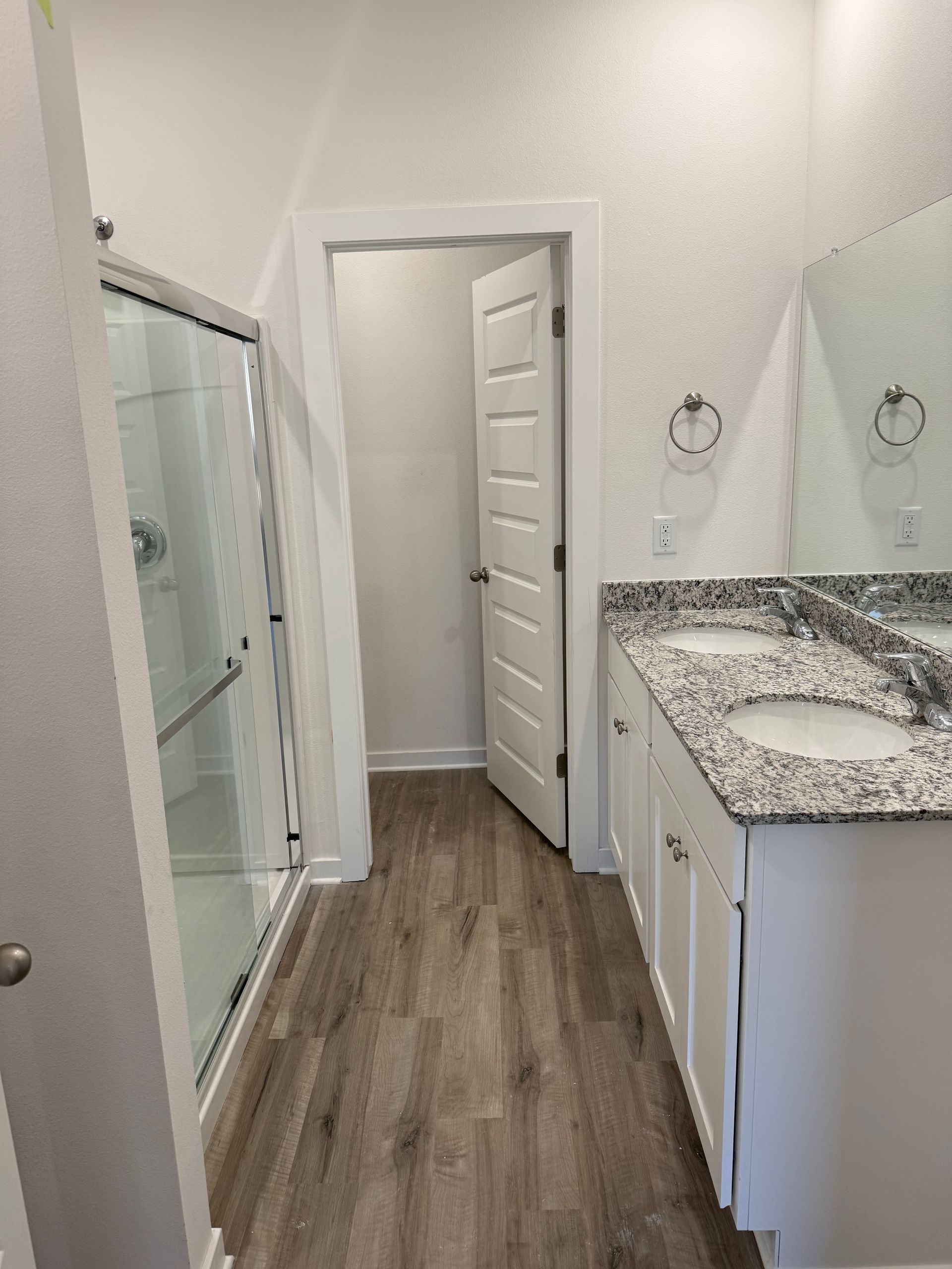 Bathroom with white cabinetry, granite countertop, glass shower, open door.