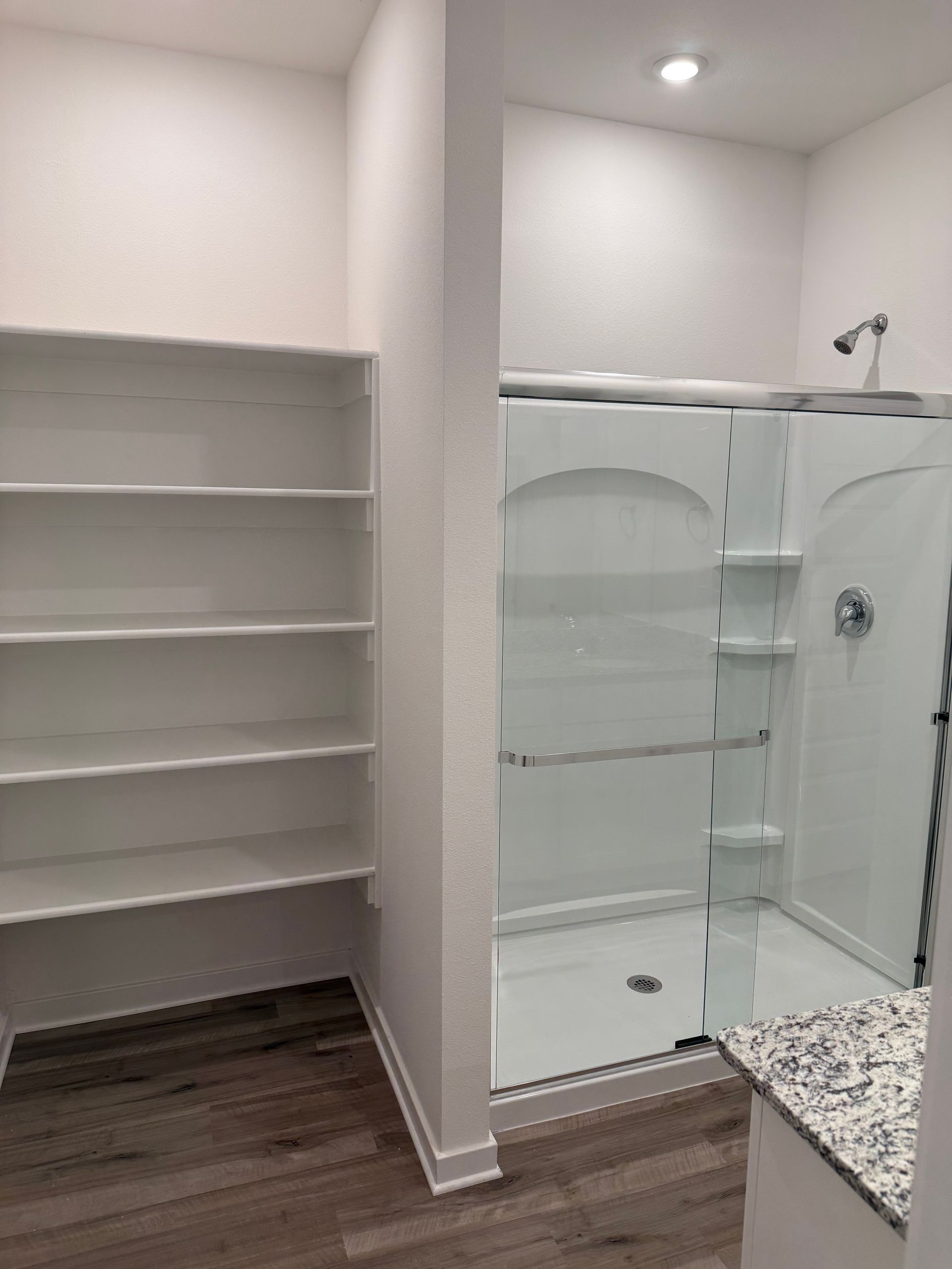 Bathroom with a walk-in shower and built-in shelves. Gray floor, white walls, and a glass shower door.