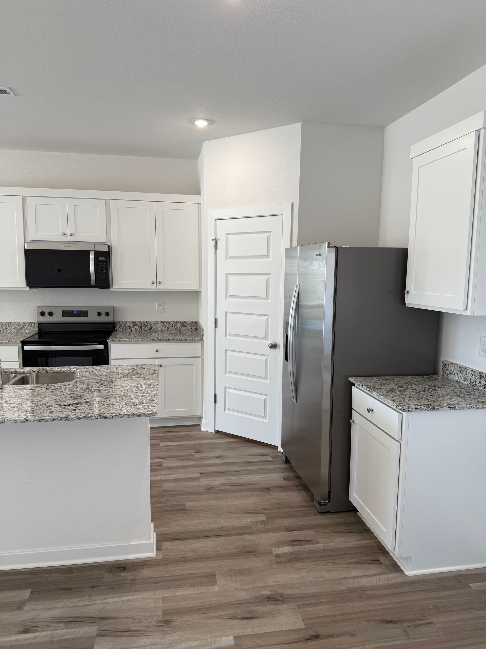 White kitchen with granite countertops, stainless steel appliances, and wood-look flooring.