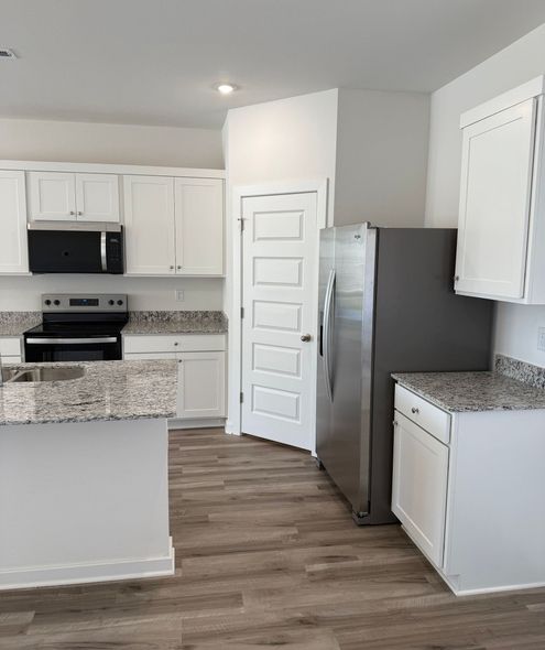 Bright kitchen with white cabinets, stainless steel refrigerator, granite countertops, and wood-look flooring.