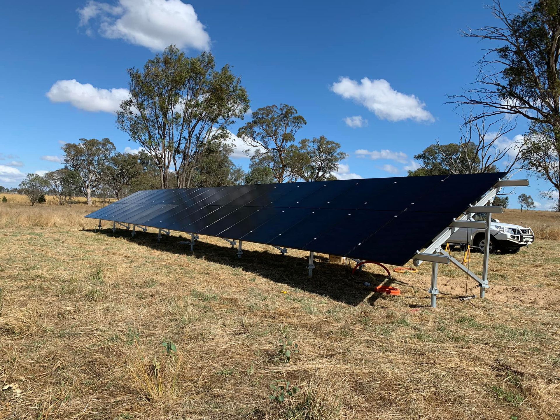 Long row of black solar panels in a dry field under a blue sky, with a truck nearby