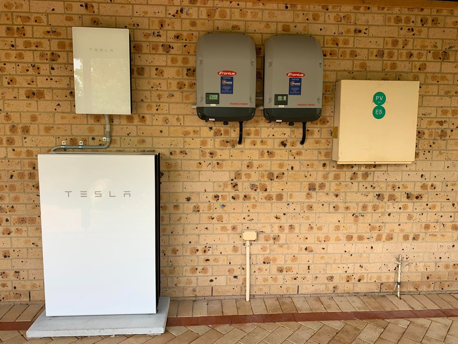 Outdoor brick wall with electrical boxes, a white cabinet, and utility meters mounted on the facade