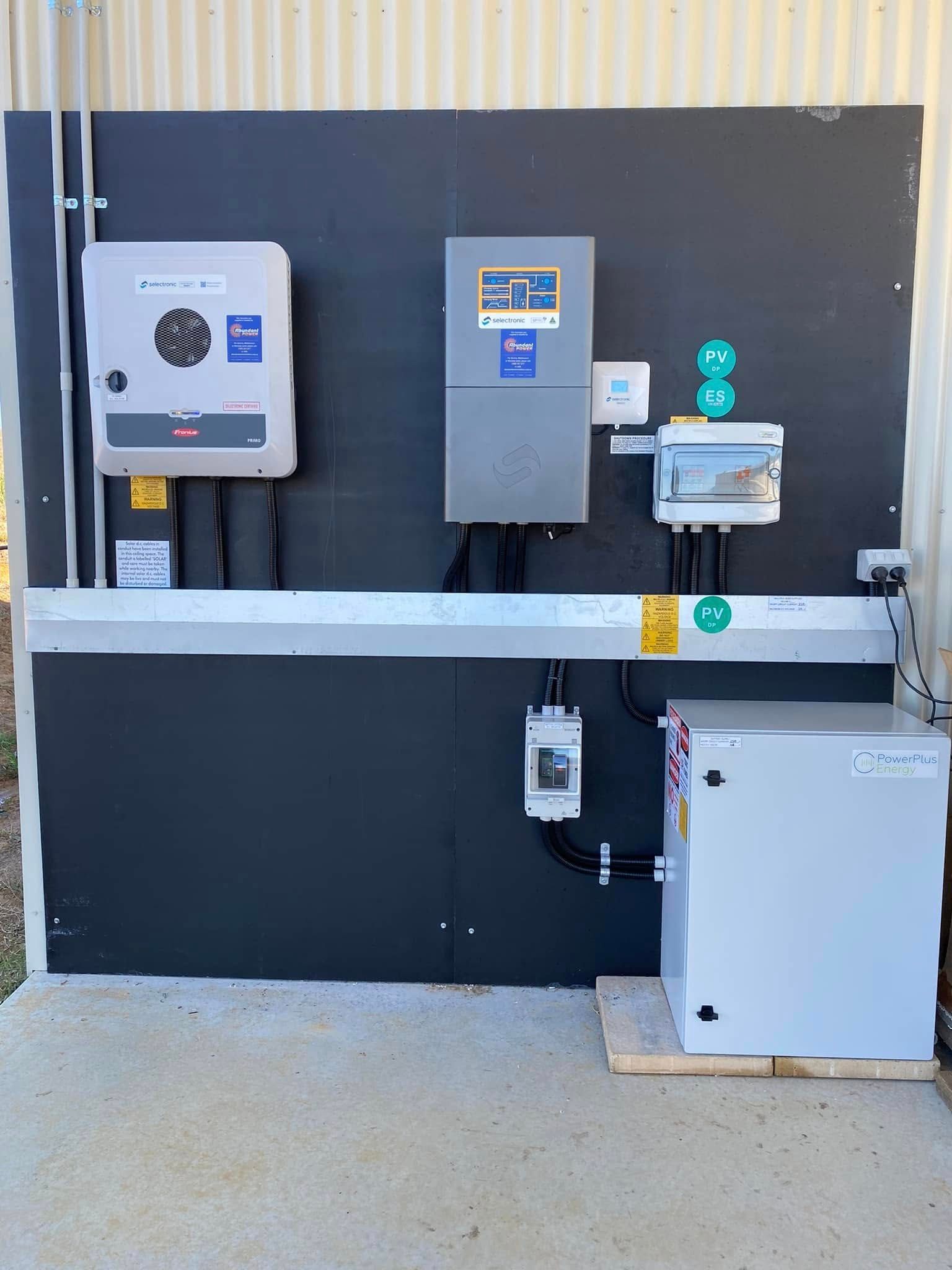 Wall-mounted electrical control panels and equipment on a black backing board in an outdoor utility area