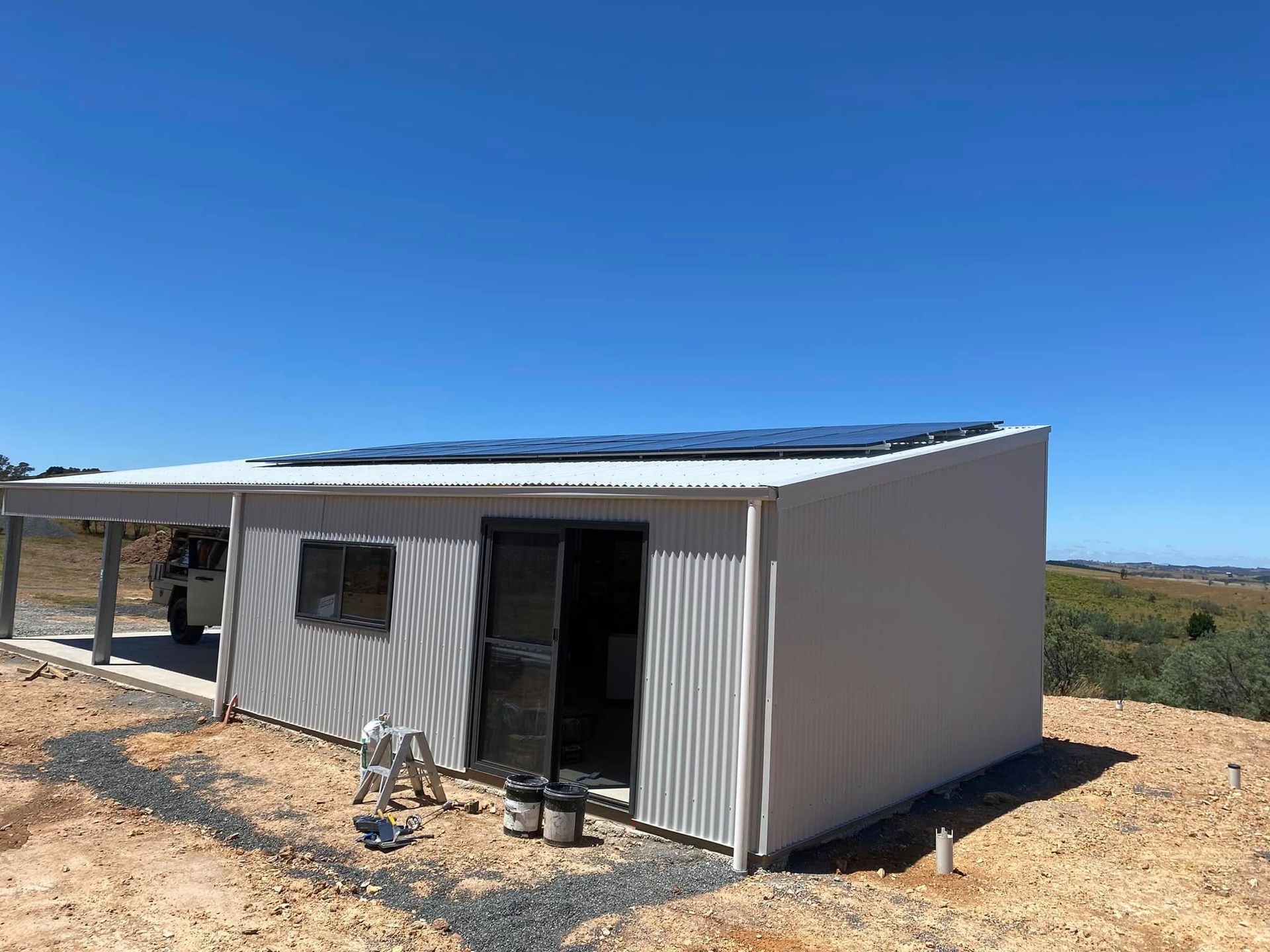 Small white metal shed with open door on a dusty rural lot under a clear blue sky.