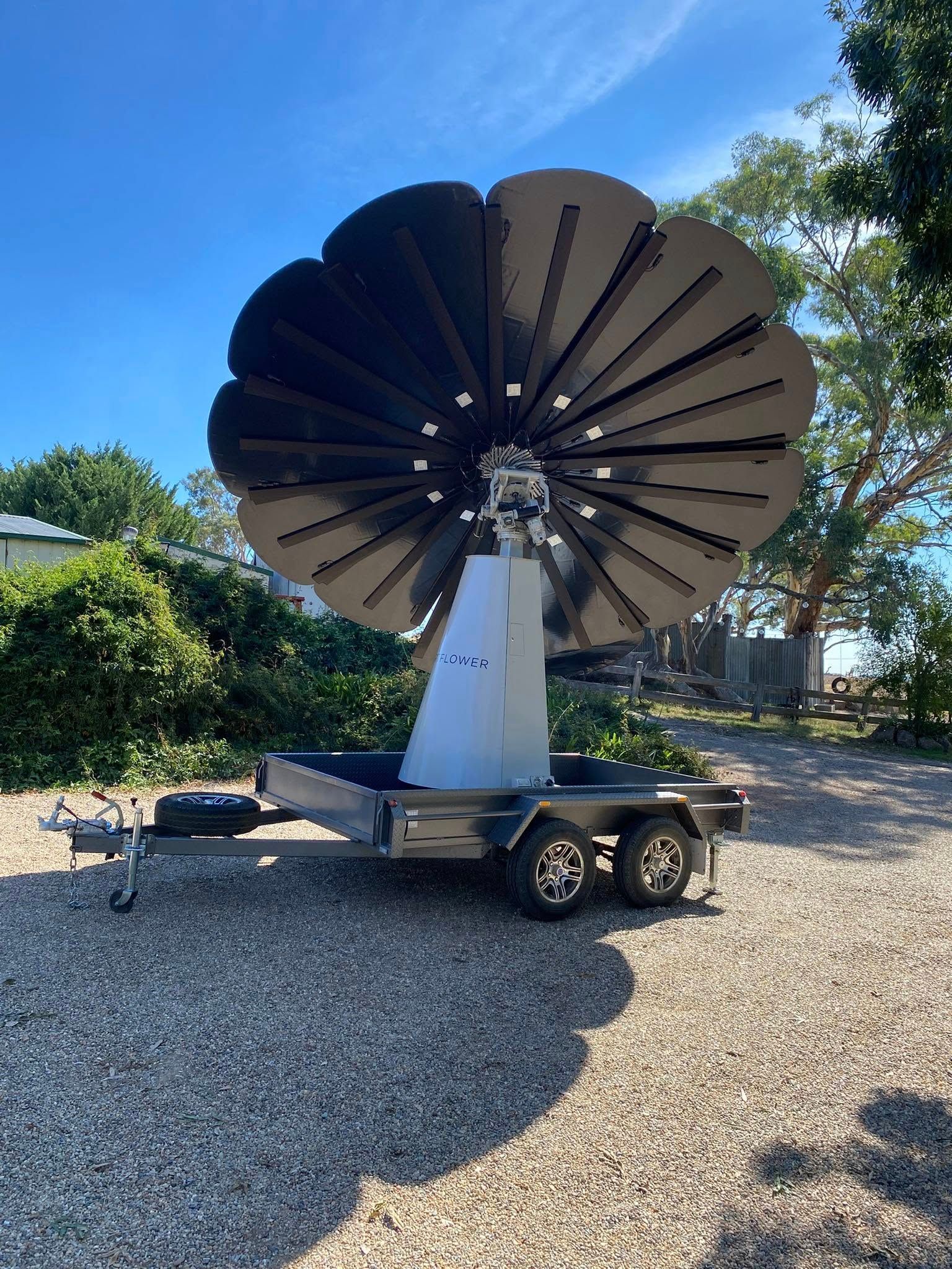 Large black wind turbine on a white trailer in a gravel yard under a blue sky.