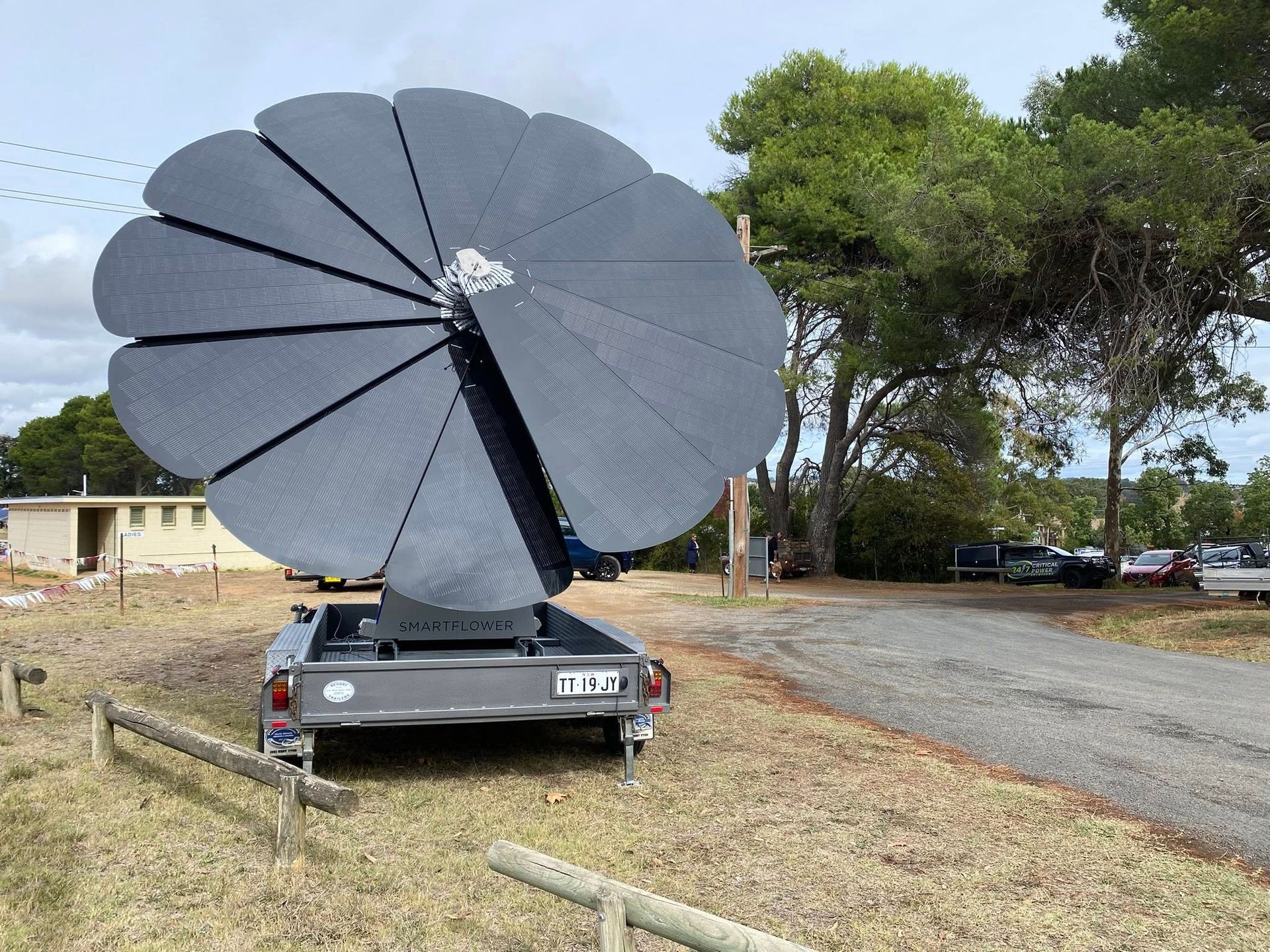 Large black satellite dish mounted on a car in a grassy outdoor area near trees and a road