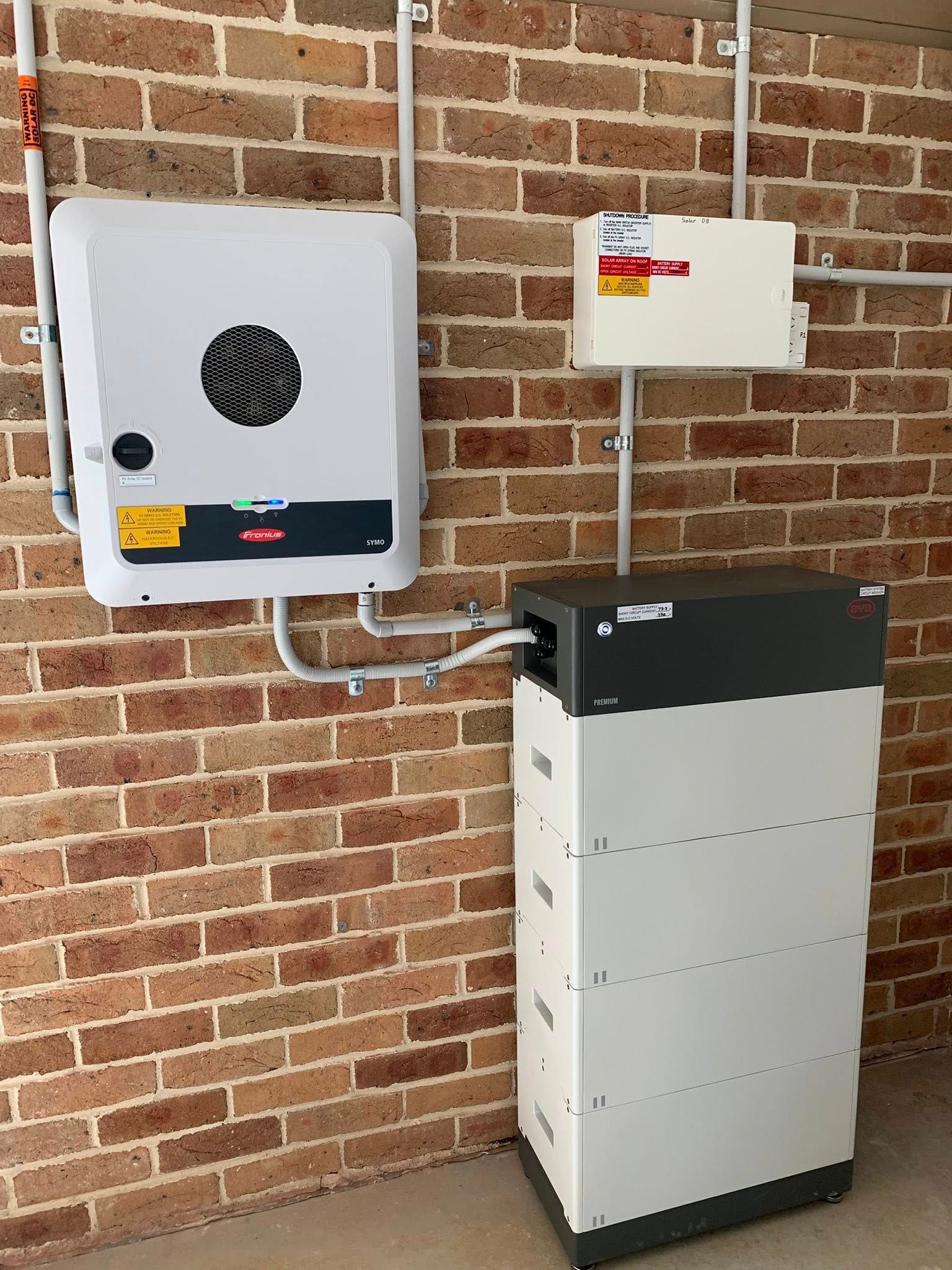 Wall-mounted and floor-standing electrical units connected by conduit on a brick exterior wall