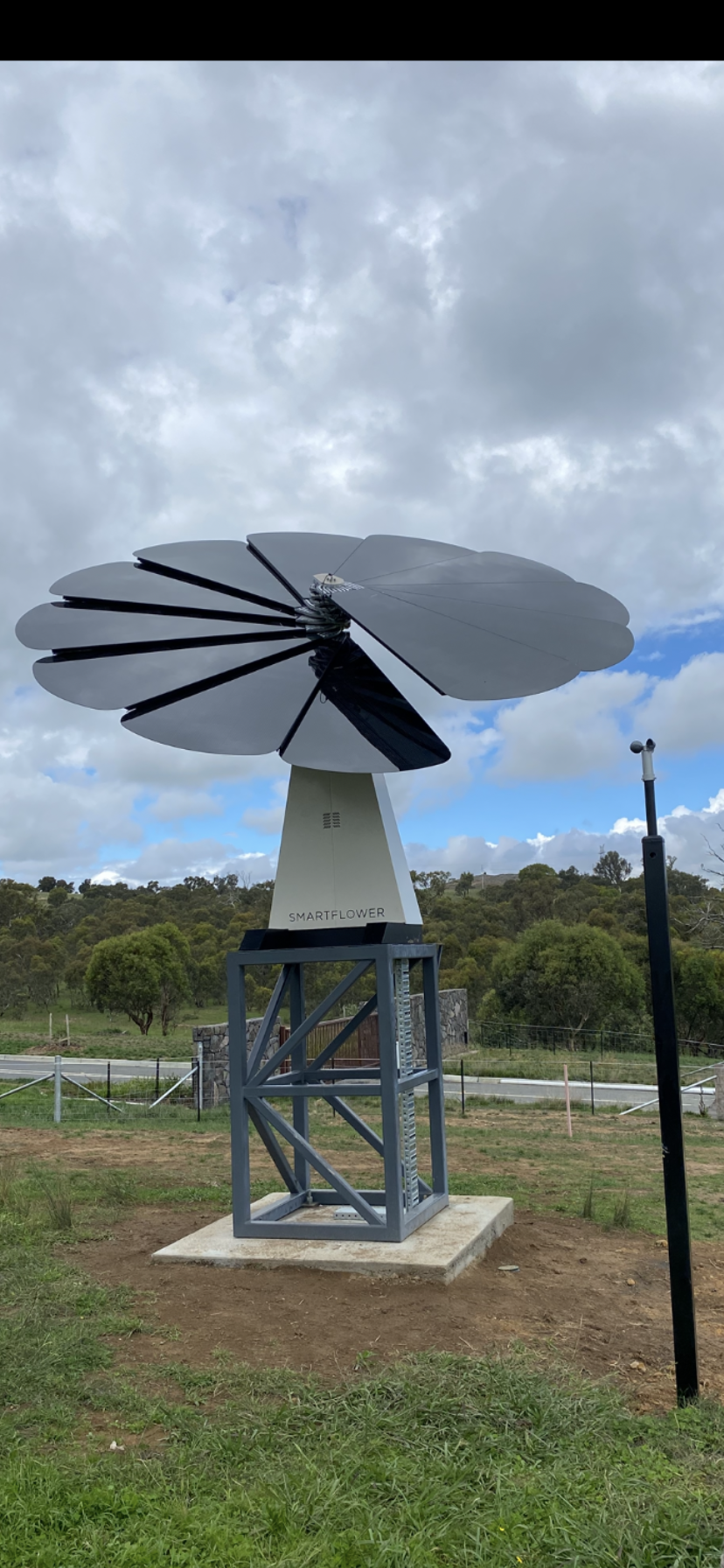 Large white and black wind turbine on a metal stand under cloudy sky in a grassy field