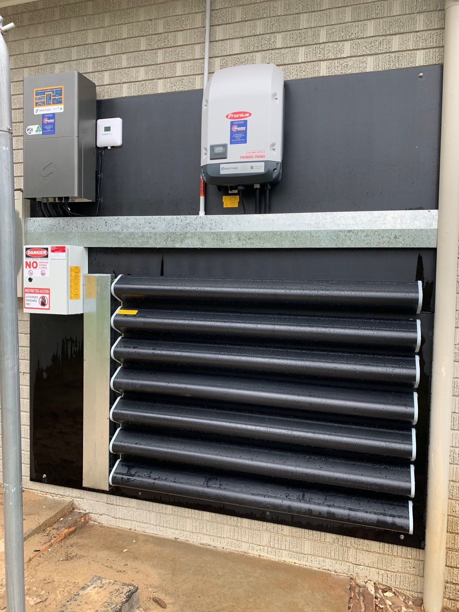 Industrial wall with electrical boxes and a large black louvered vent on a brick exterior.