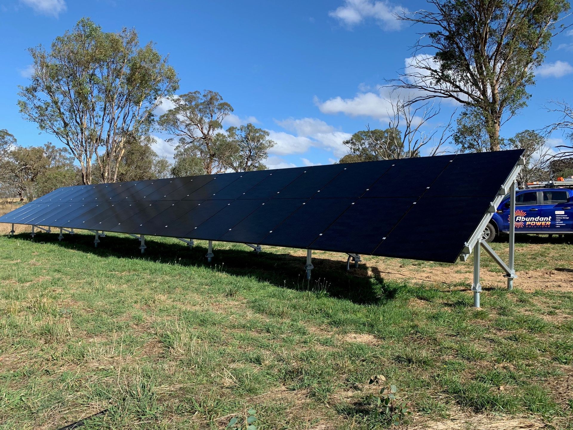 Long black solar panel array on a grassy field under a blue sky