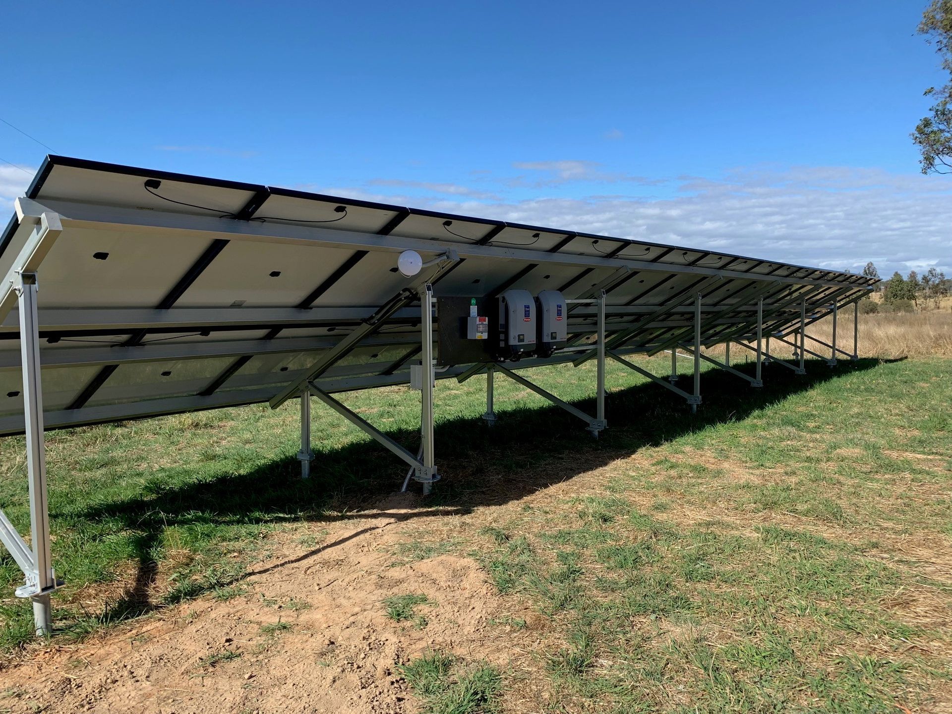 Row of solar panels on metal frames in a grassy field under a blue sky