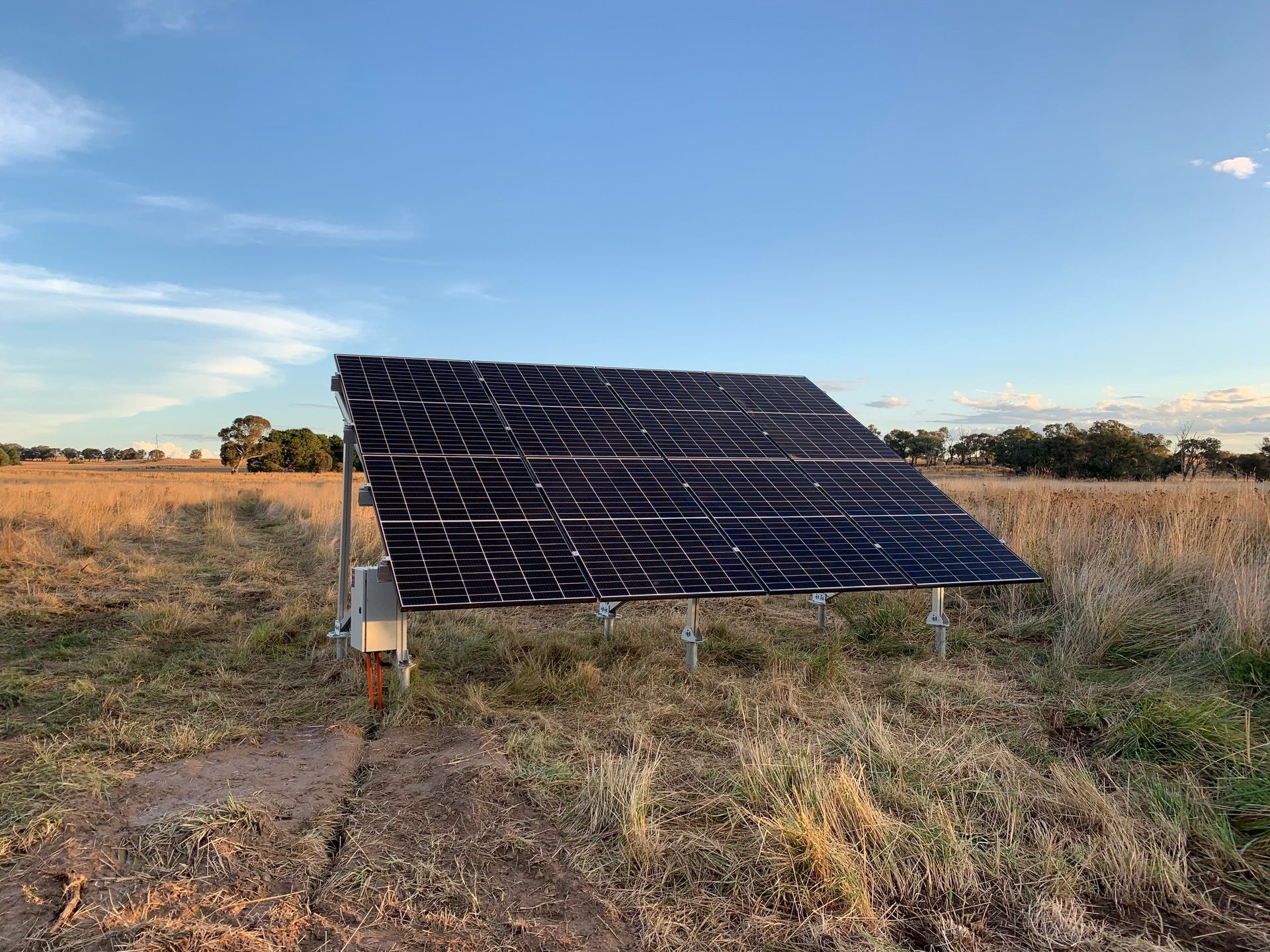 Solar panel array on metal supports in a grassy field under a clear blue sky.