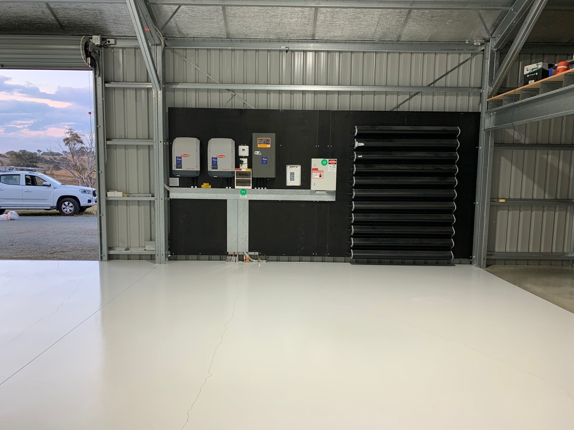 Empty warehouse interior with gray walls, control panels, and a black roller door on the right.