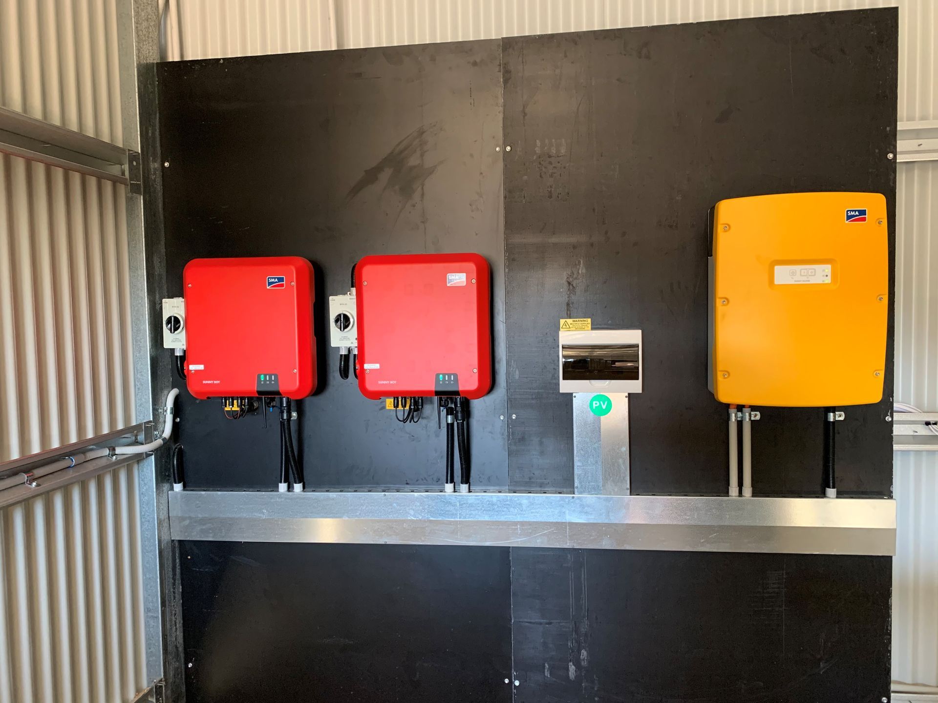 Three wall-mounted electrical boxes—two red and one yellow—on a black wall in an industrial space