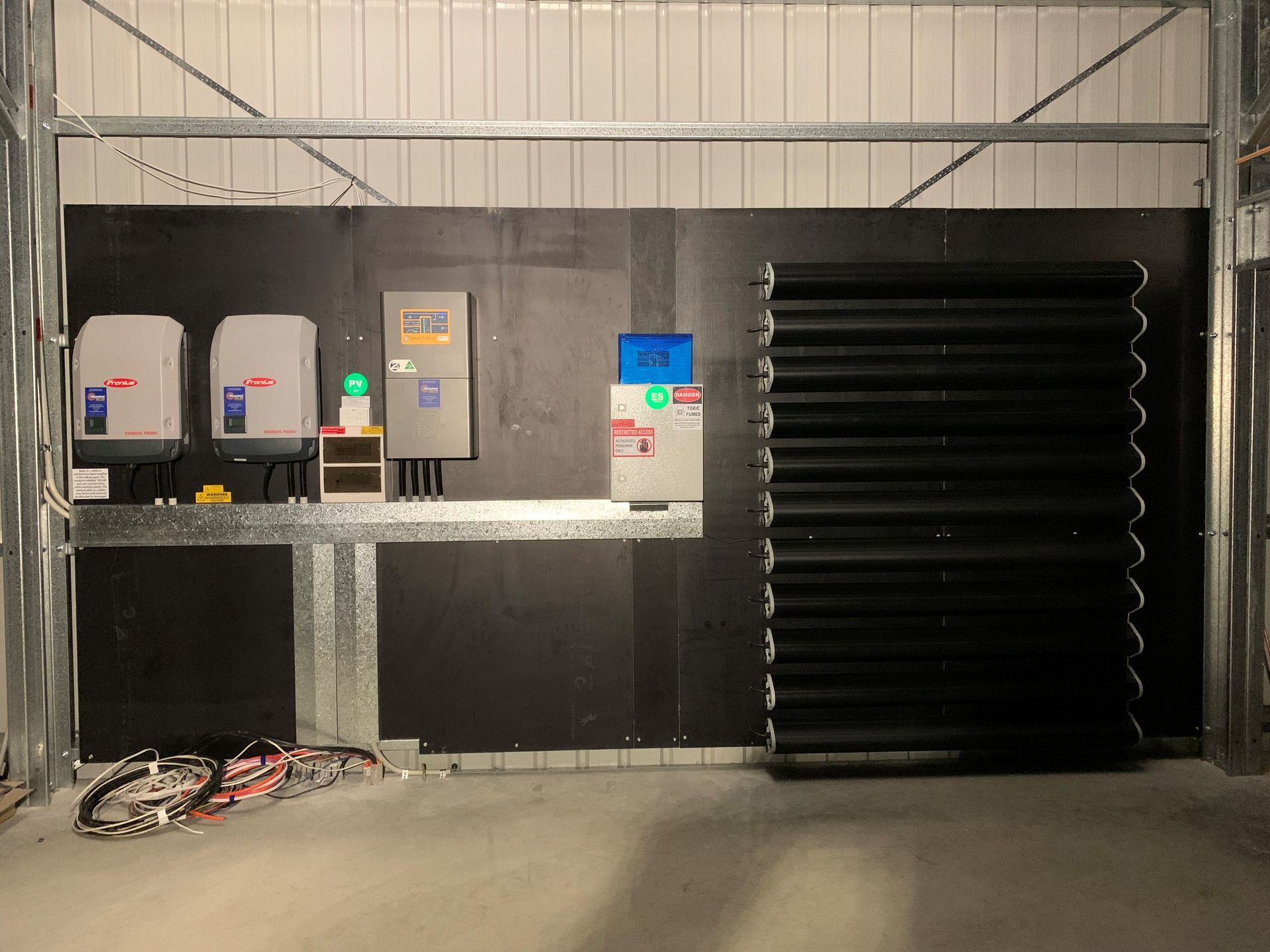 Industrial utility room with three electrical cabinets, a control panel, and a large black cooling unit