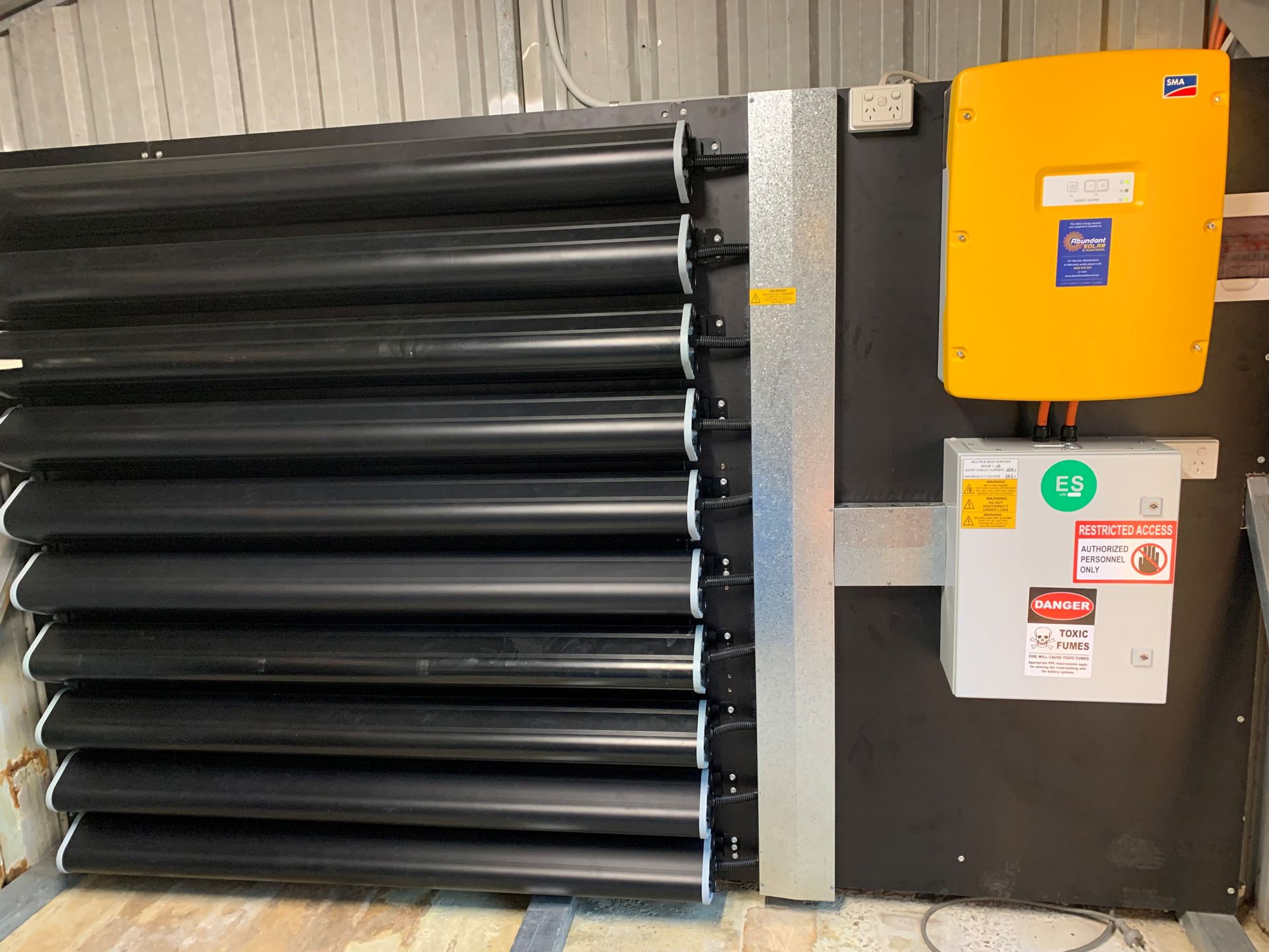 Black industrial louvered vent beside a yellow electrical control box on a wall