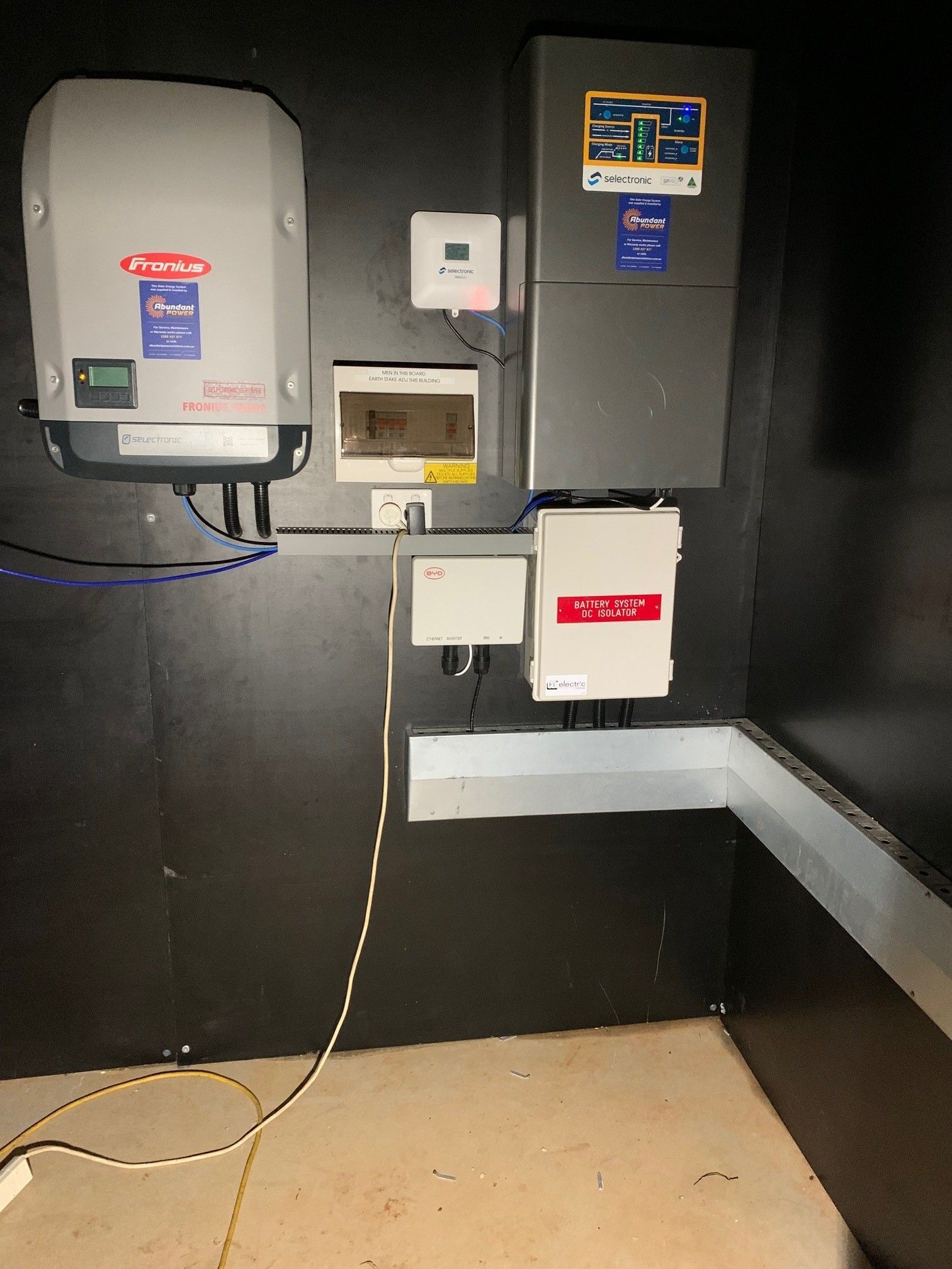 Electrical control panels mounted on a dark wall in a utility room with exposed wiring and conduit.