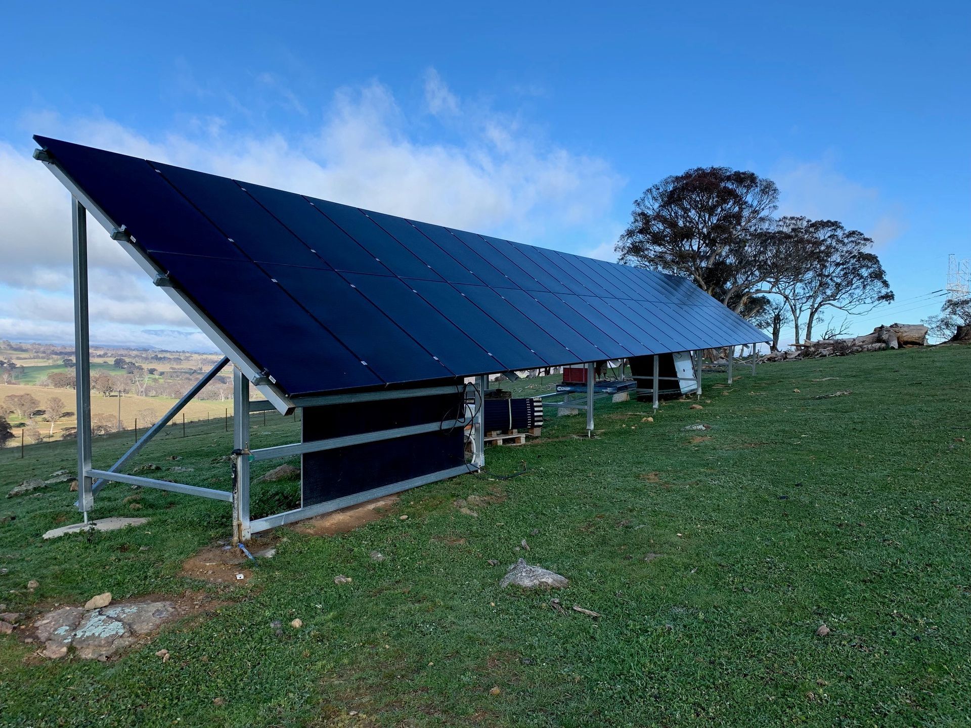 Large blue solar panel array on a grassy hillside under a clear sky