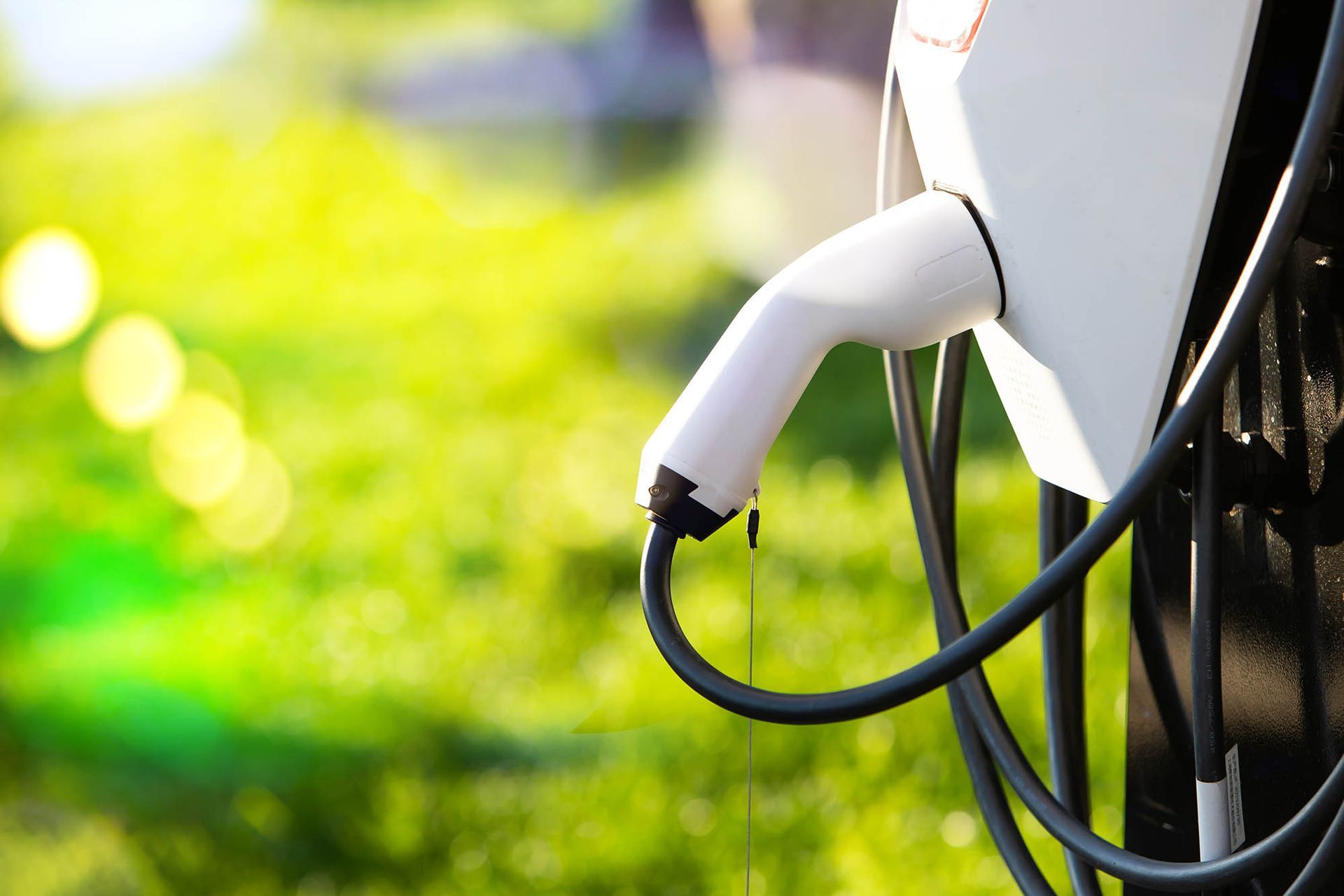 Electric vehicle charging plug connected to a car, with blurred green background