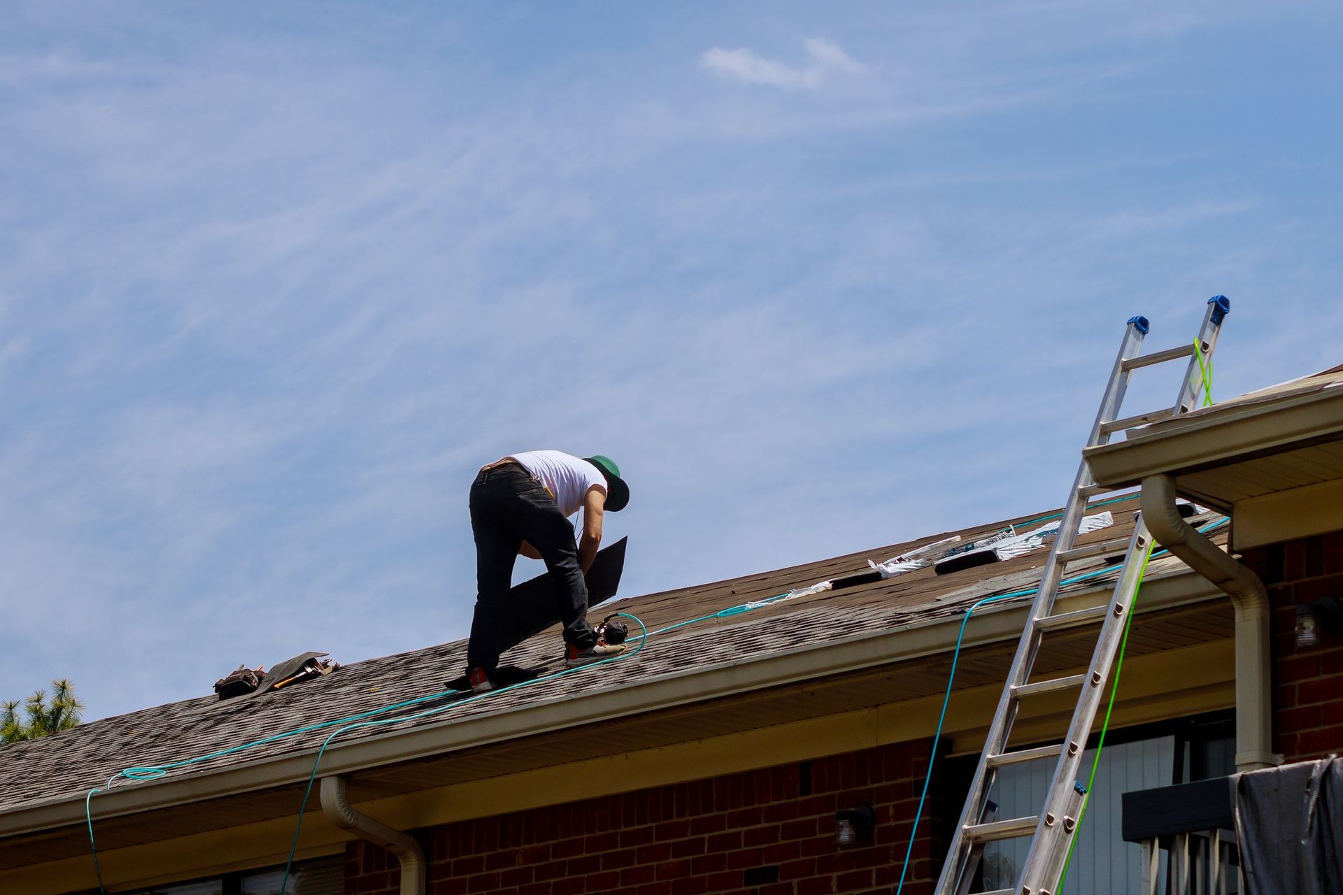 Worker repairing a roof beside a ladder under a clear blue sky