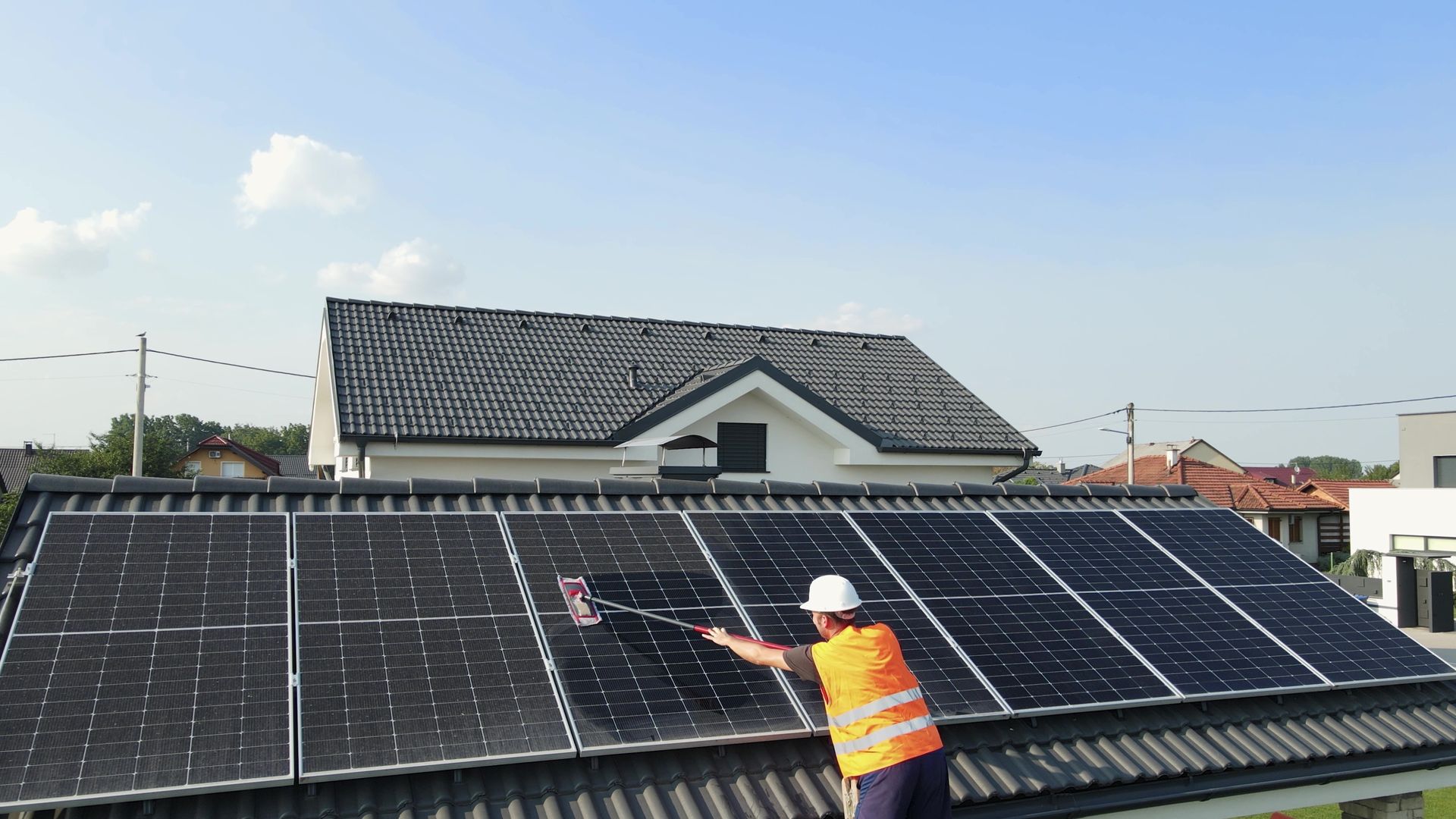 Worker in orange vest installing solar panels on a rooftop under a blue sky.