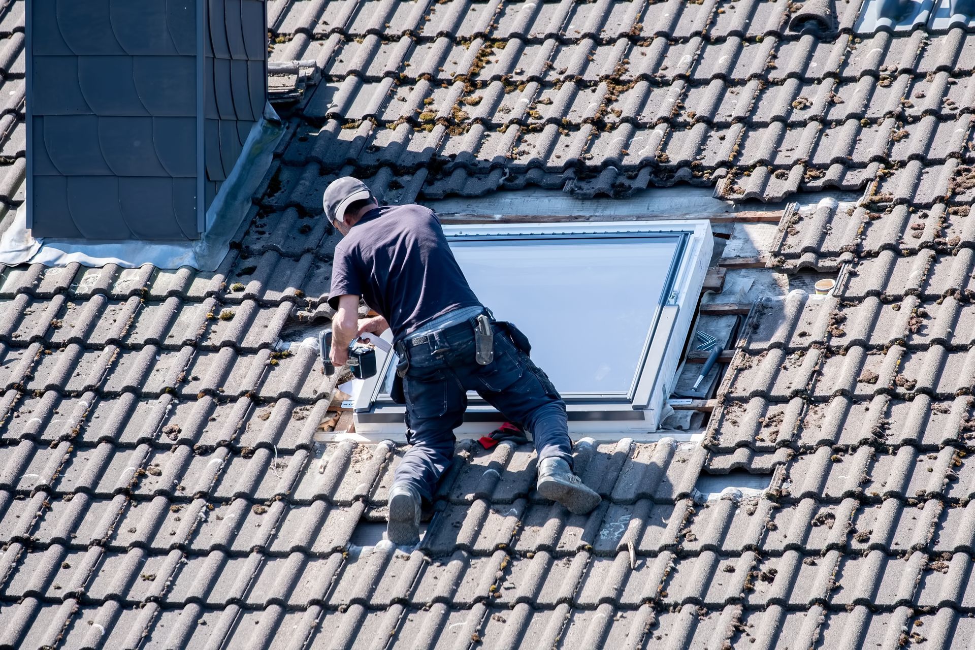 Worker repairing a skylight on a tiled roof near a chimney