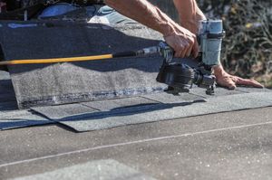 Worker using a nail gun to secure roofing shingles on a rooftop