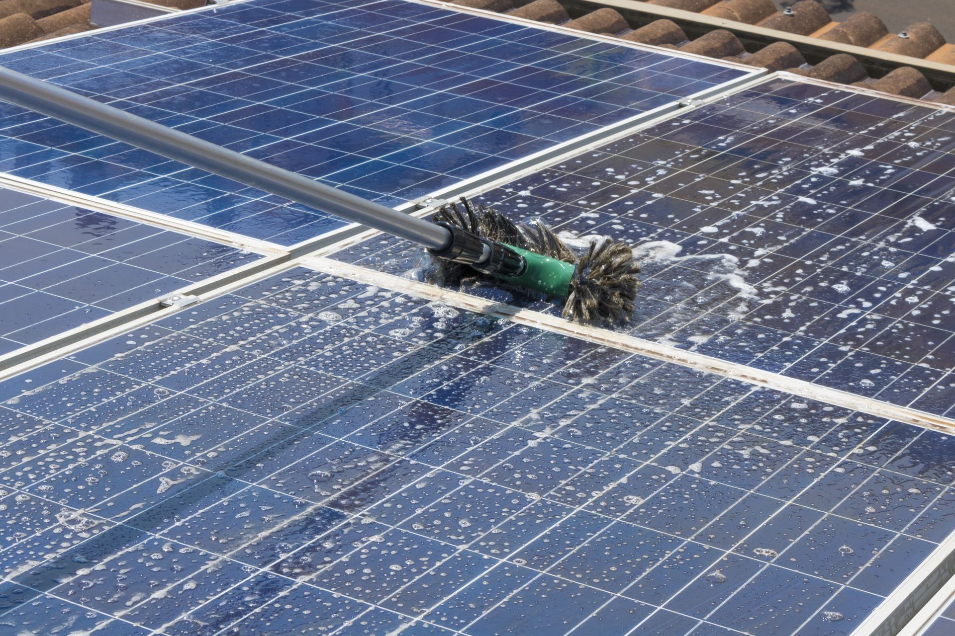 Robotic cleaner moving across blue solar panels, spraying water and foam