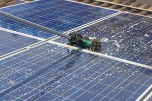 Robotic cleaner moving across blue solar panels, spraying water and foam