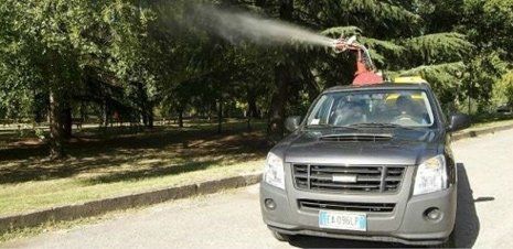 Un camion argentato spruzza acqua da un tubo montato sul tetto su una strada alberata.