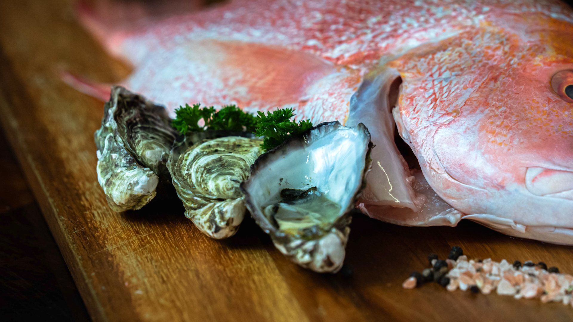 A fish and oysters are on a wooden cutting board.