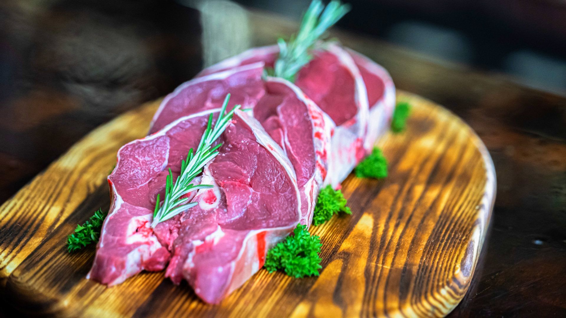 Two raw steaks are sitting on a wooden cutting board.