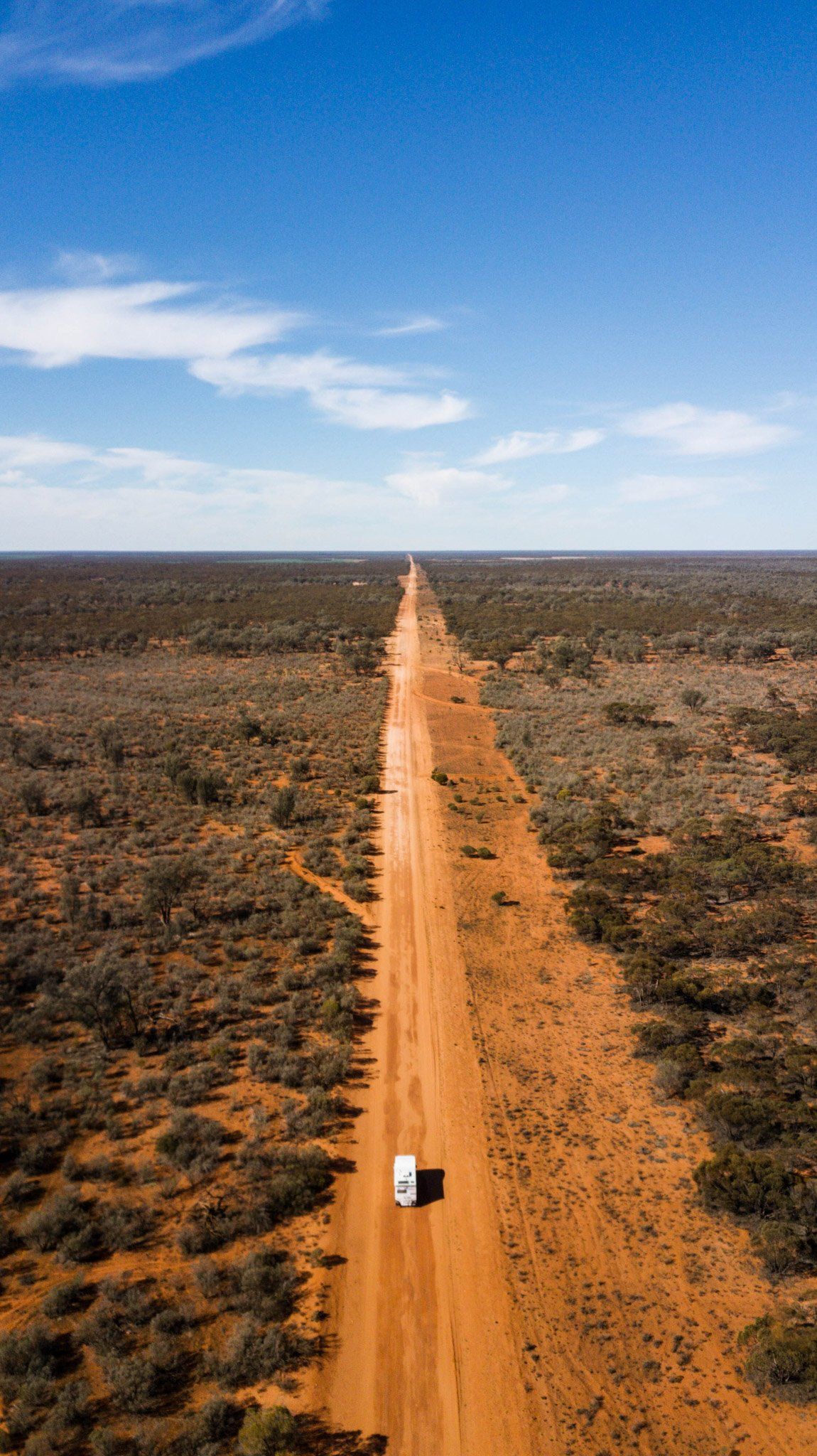 An aerial view of a truck driving down a dirt road in the desert.