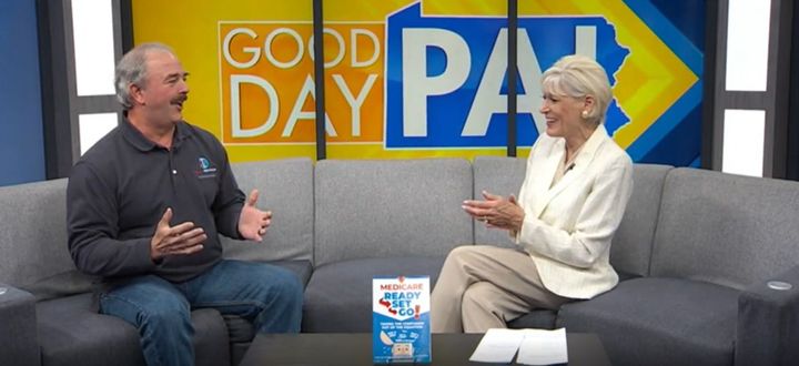 A man and a woman sitting on a couch on the set of Good Day PA, with a book placed on the coffee table in front of them.