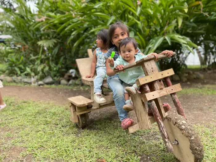 Children playing on a handmade wooden bike toy outdoors at Casa Agua Azul
