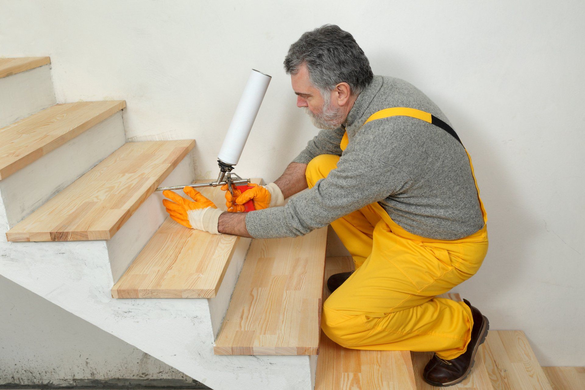 Man in yellow overalls applying sealant to wooden staircase.
