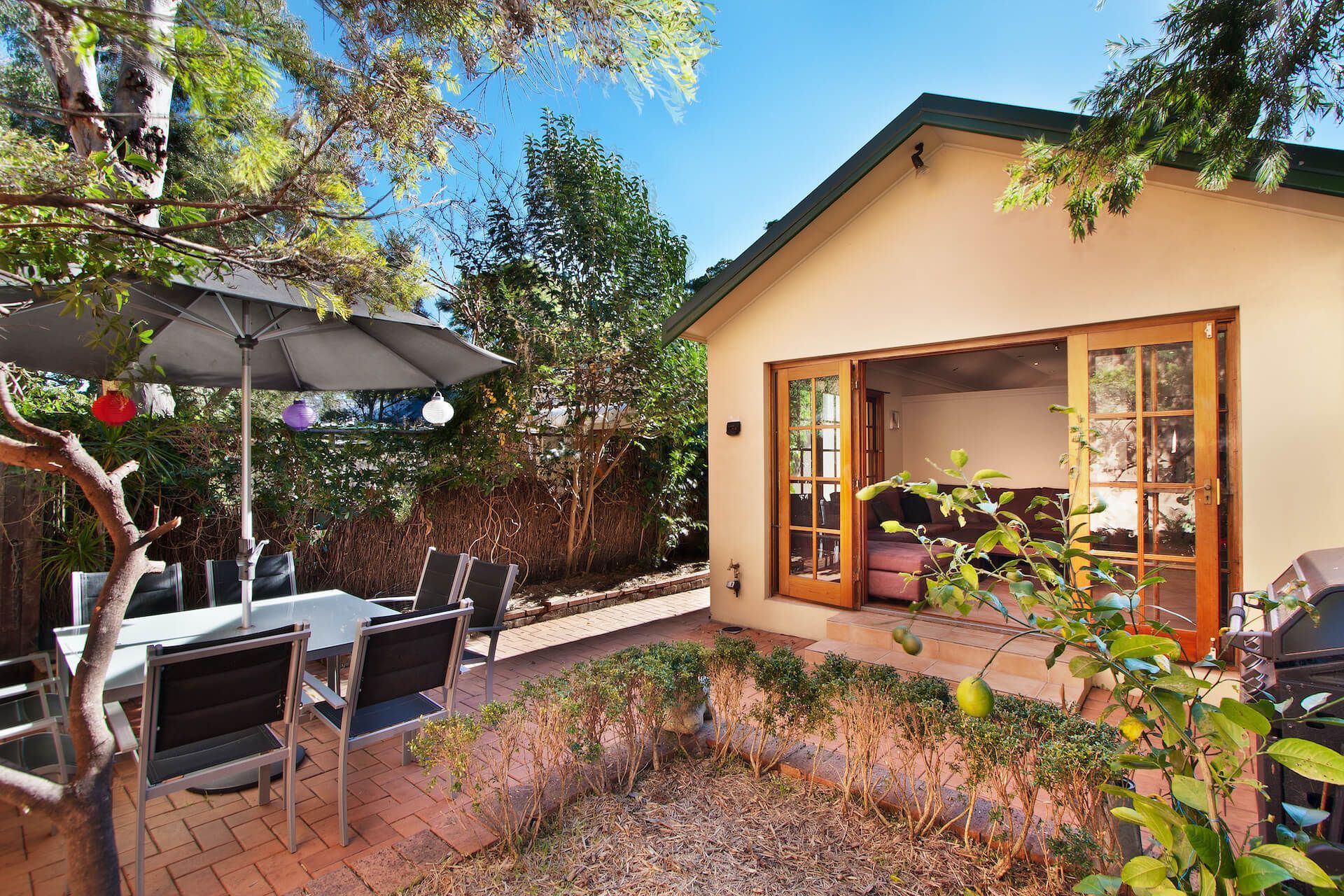 Backyard patio with table, chairs, umbrella, and a small building with open doors.
