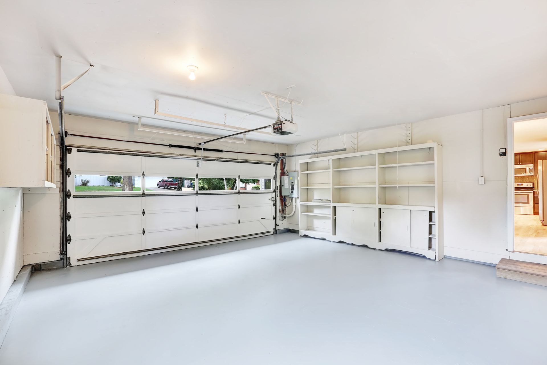 Empty, freshly painted garage interior. White walls, gray floor, built-in shelving, garage door open.