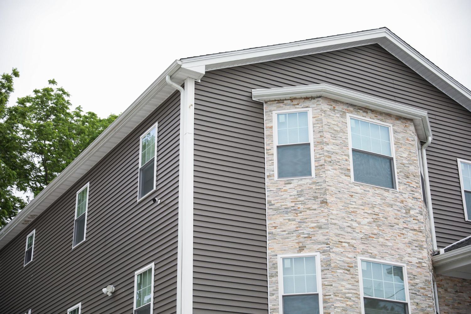 Exterior corner of a gray apartment building with stone and siding, seen from below