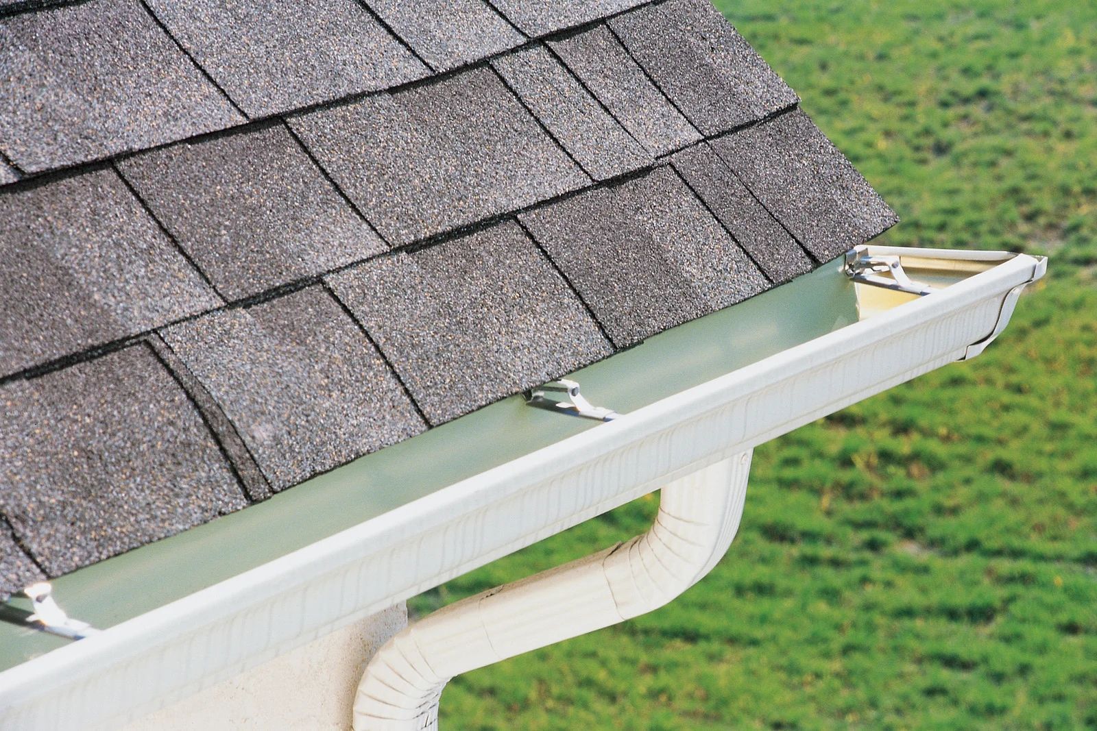 Rain gutter along a shingled roof edge beside a green lawn