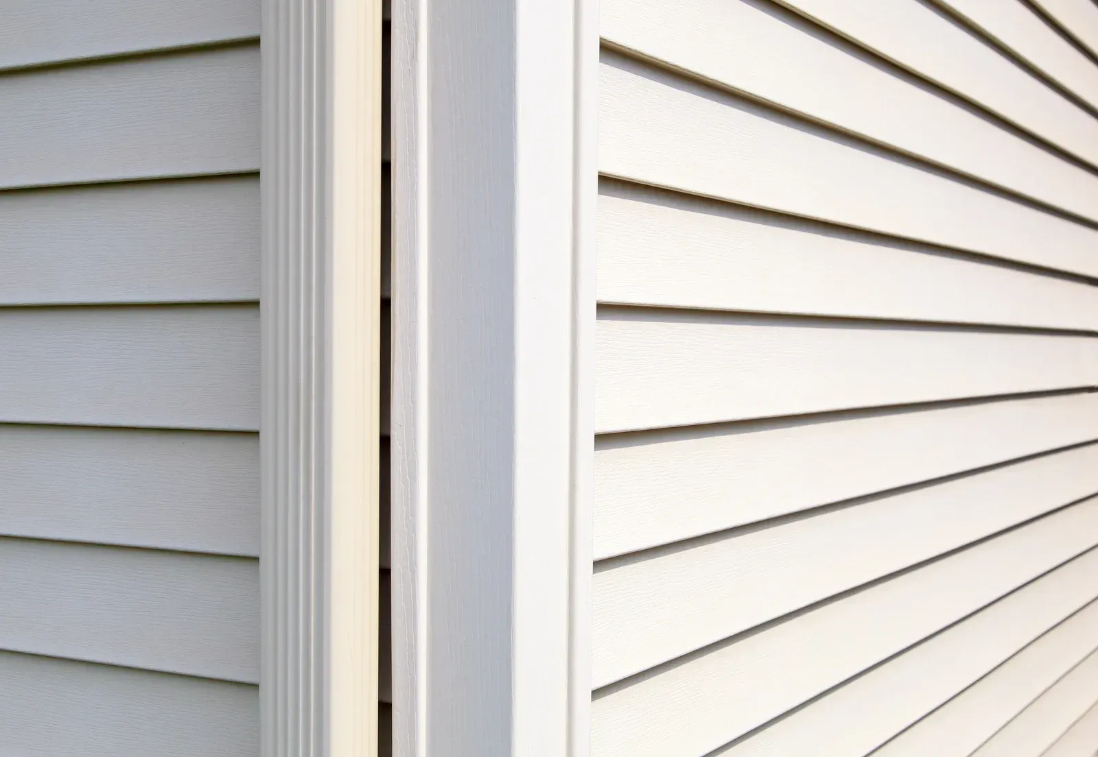 Close-up of two white-sided house corners with vertical trim and horizontal siding.