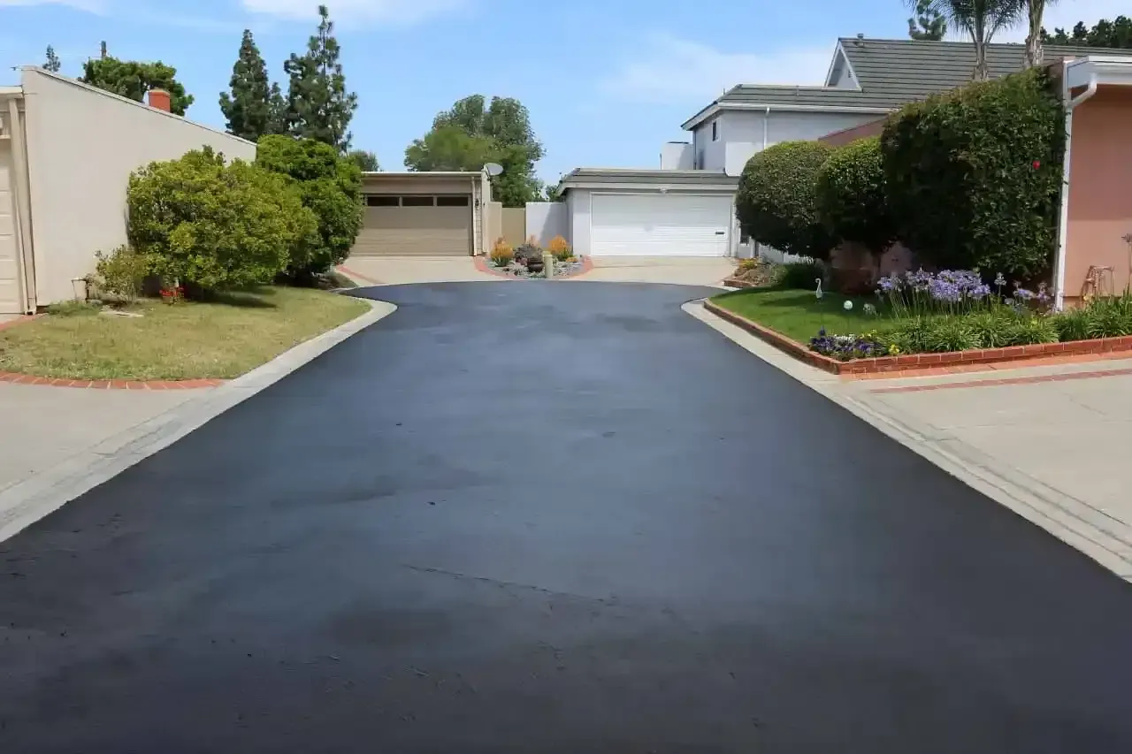 A black asphalt driveway leading to a house in a residential neighborhood.
