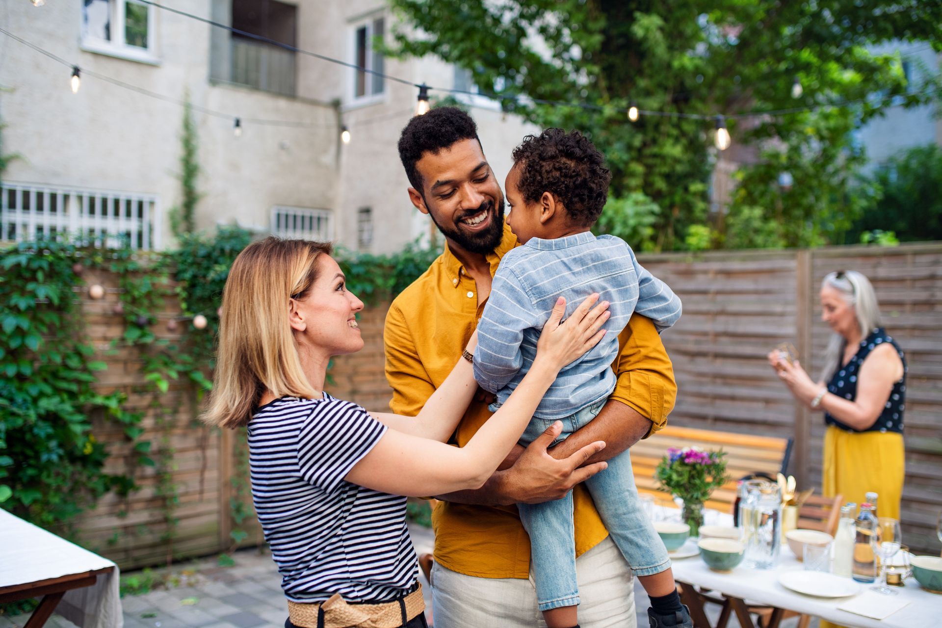 A man and woman are holding a child at a backyard party.