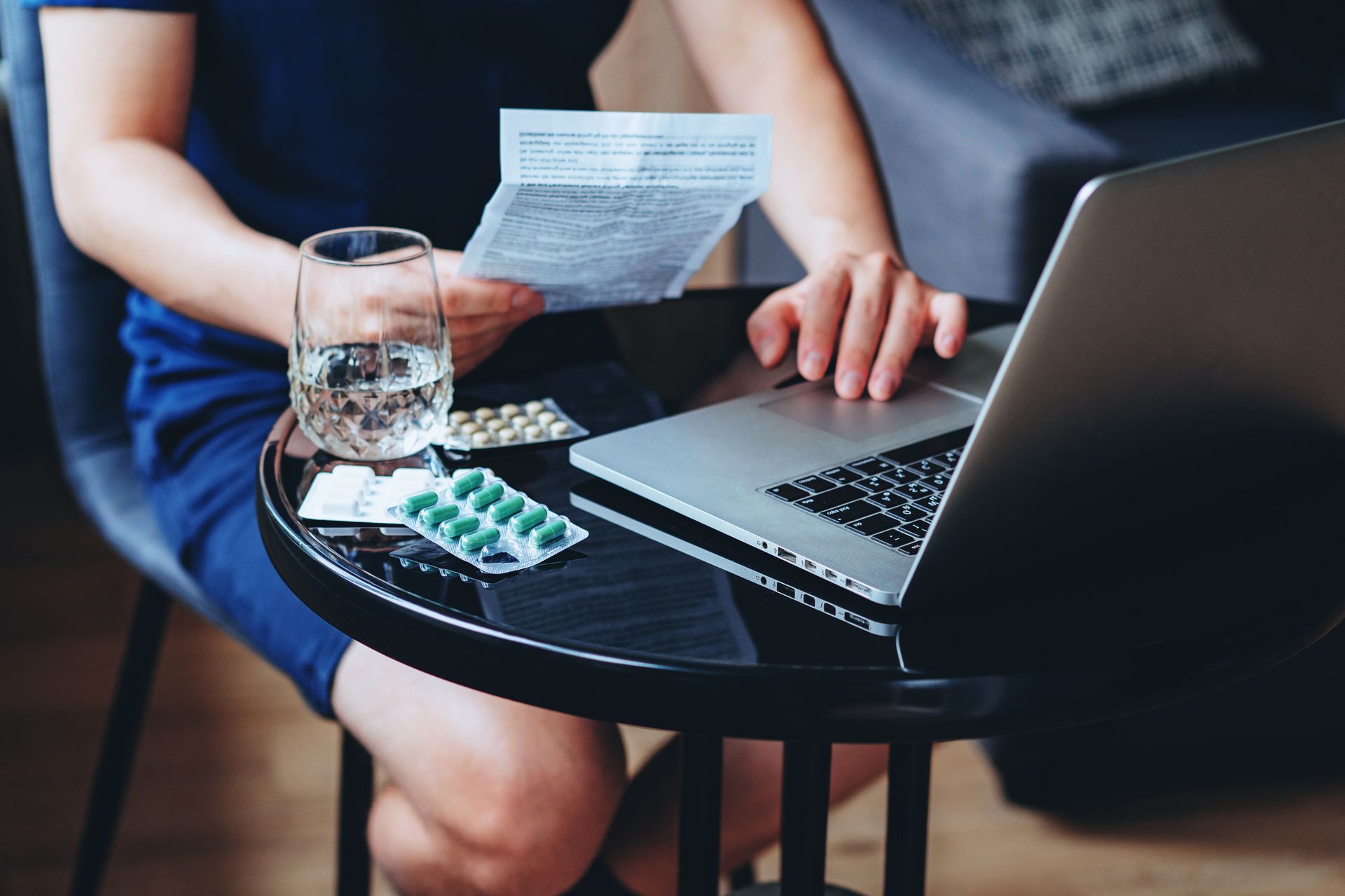 A woman is sitting at a table with a laptop and a glass of water.