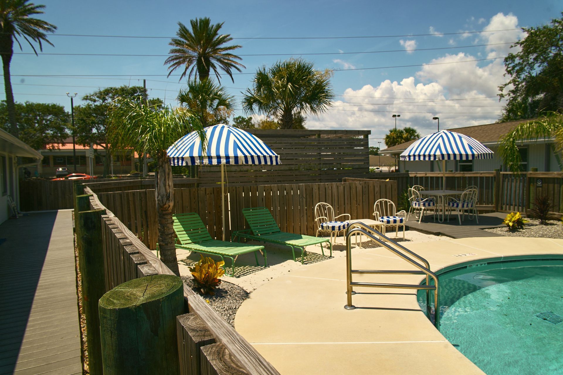 Backyard pool with lounge chairs, striped umbrellas, and palm trees under a sunny sky