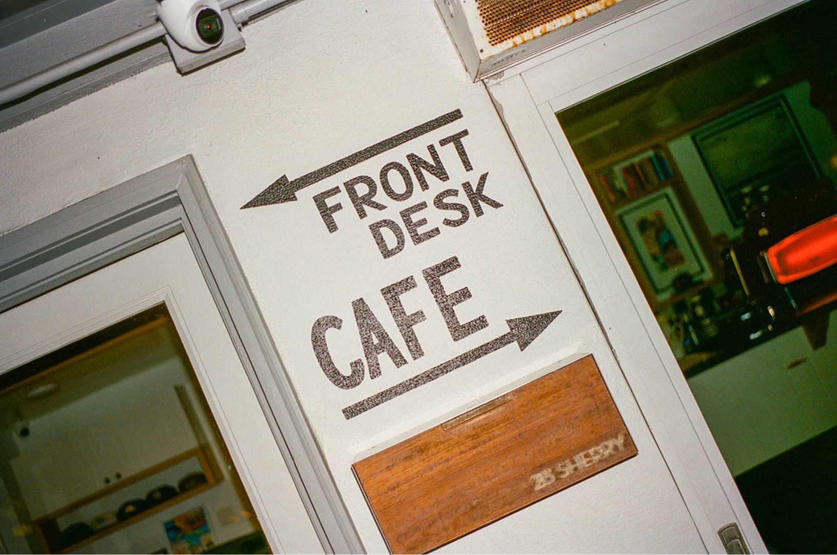 Front desk café sign on a white wall beside a window and orange menu board