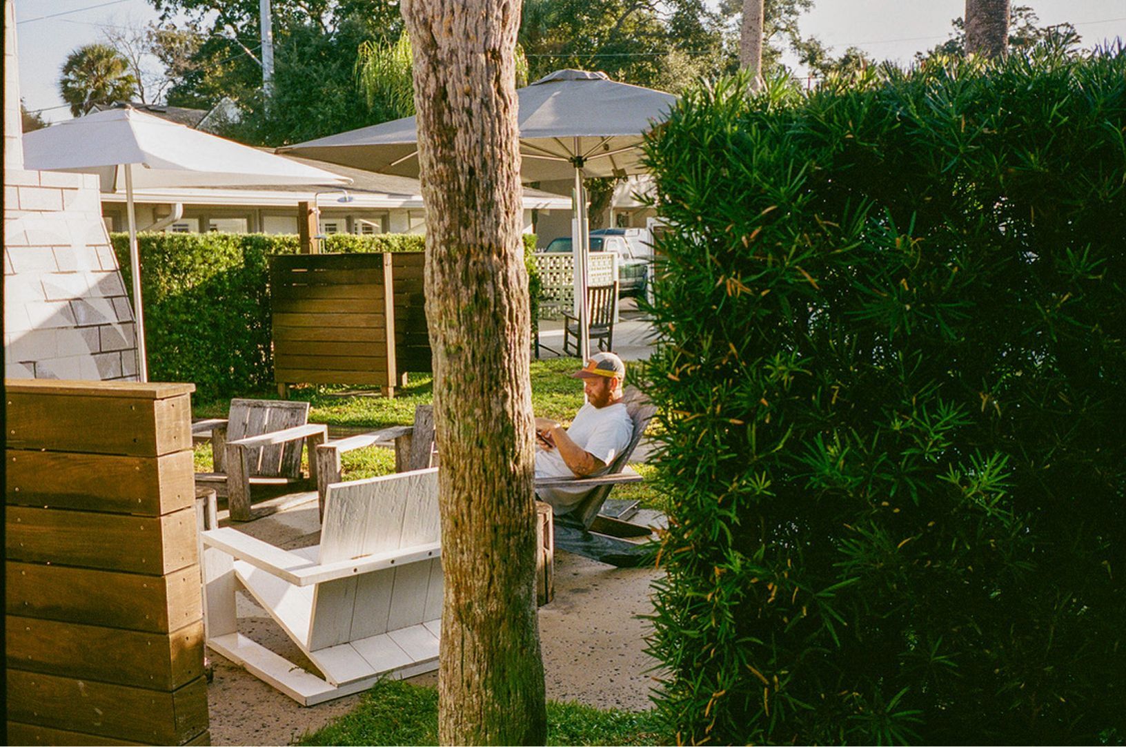 Patio seating area with white umbrellas, greenery, and a person relaxing near a wooden deck