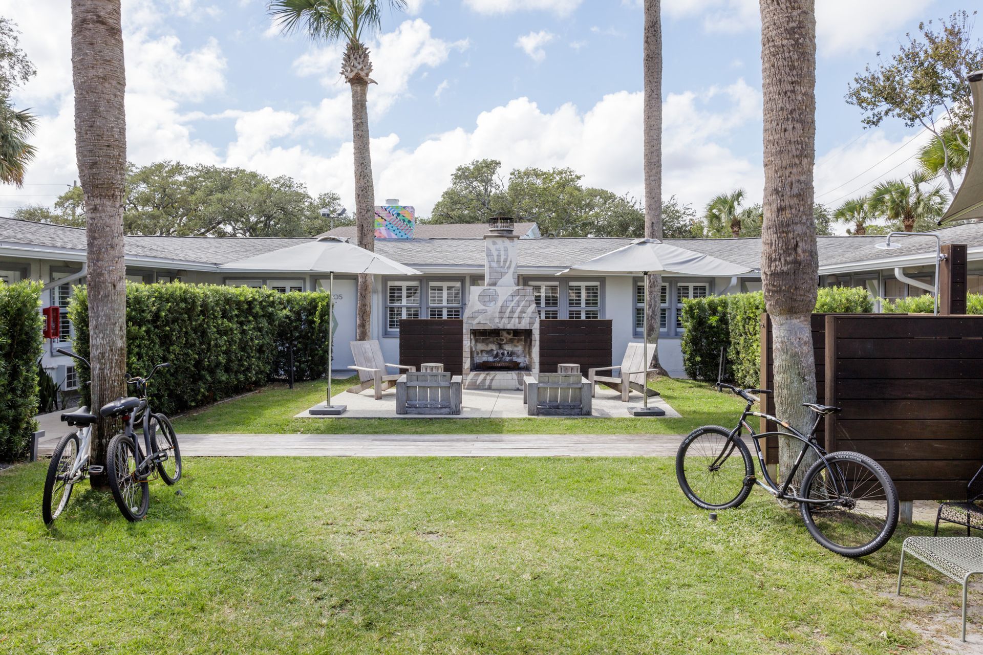 Bungalow with a front lawn, patio seating, and bicycles under tall palm trees