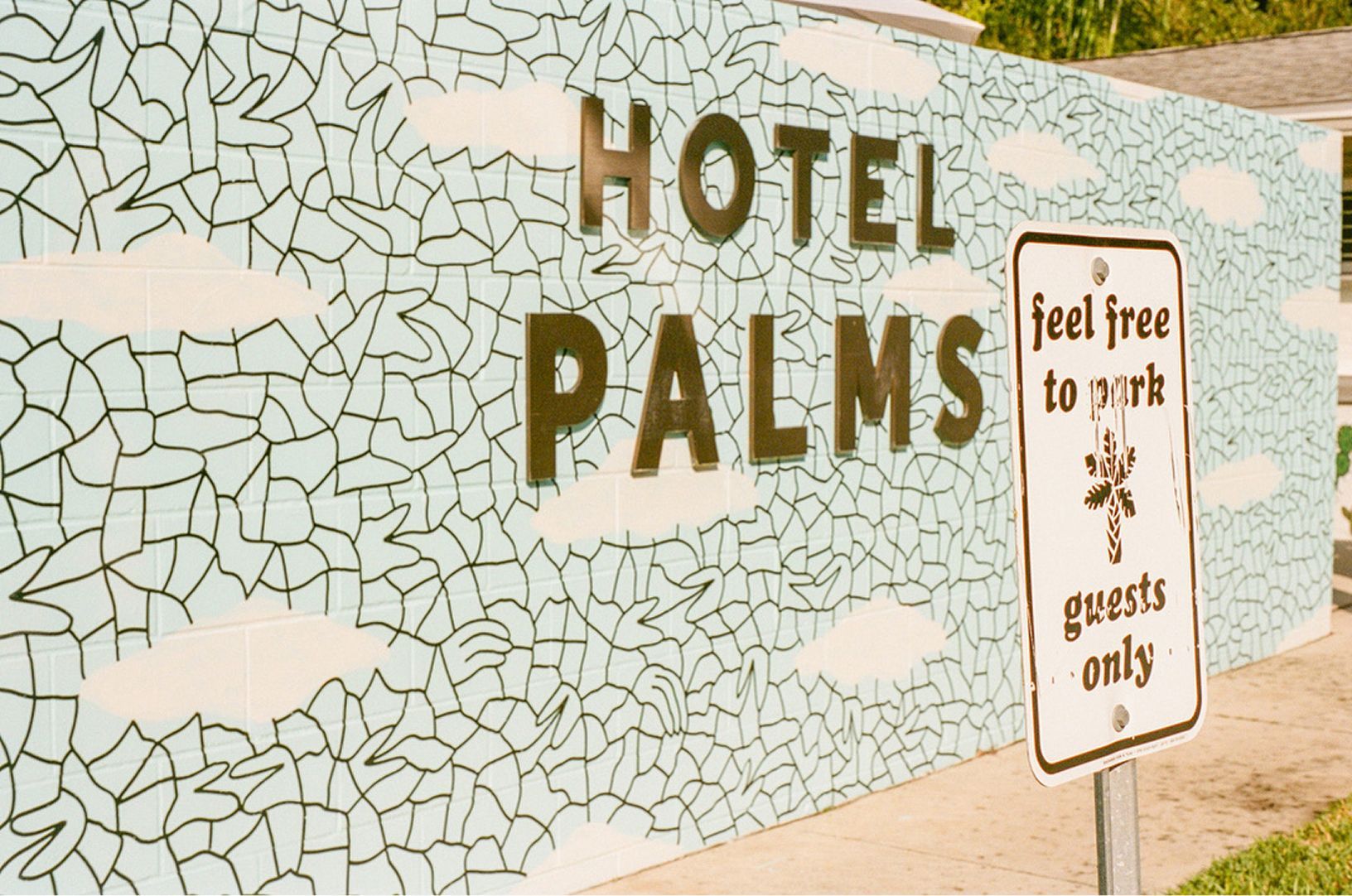 Hotel PALMS sign on a mosaic wall with a “feel free to ask guests only” sign nearby